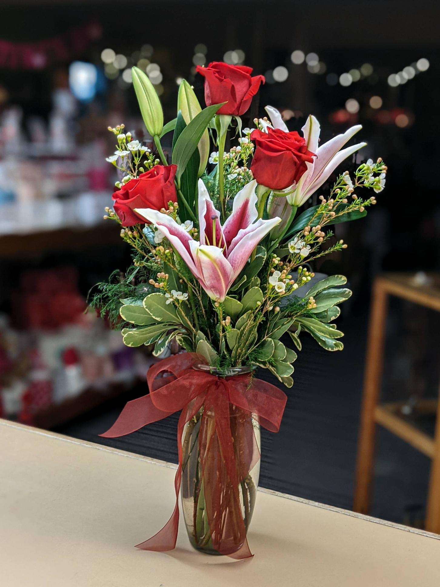 Red roses and pink lilies in a clear glass vase with a red ribbon