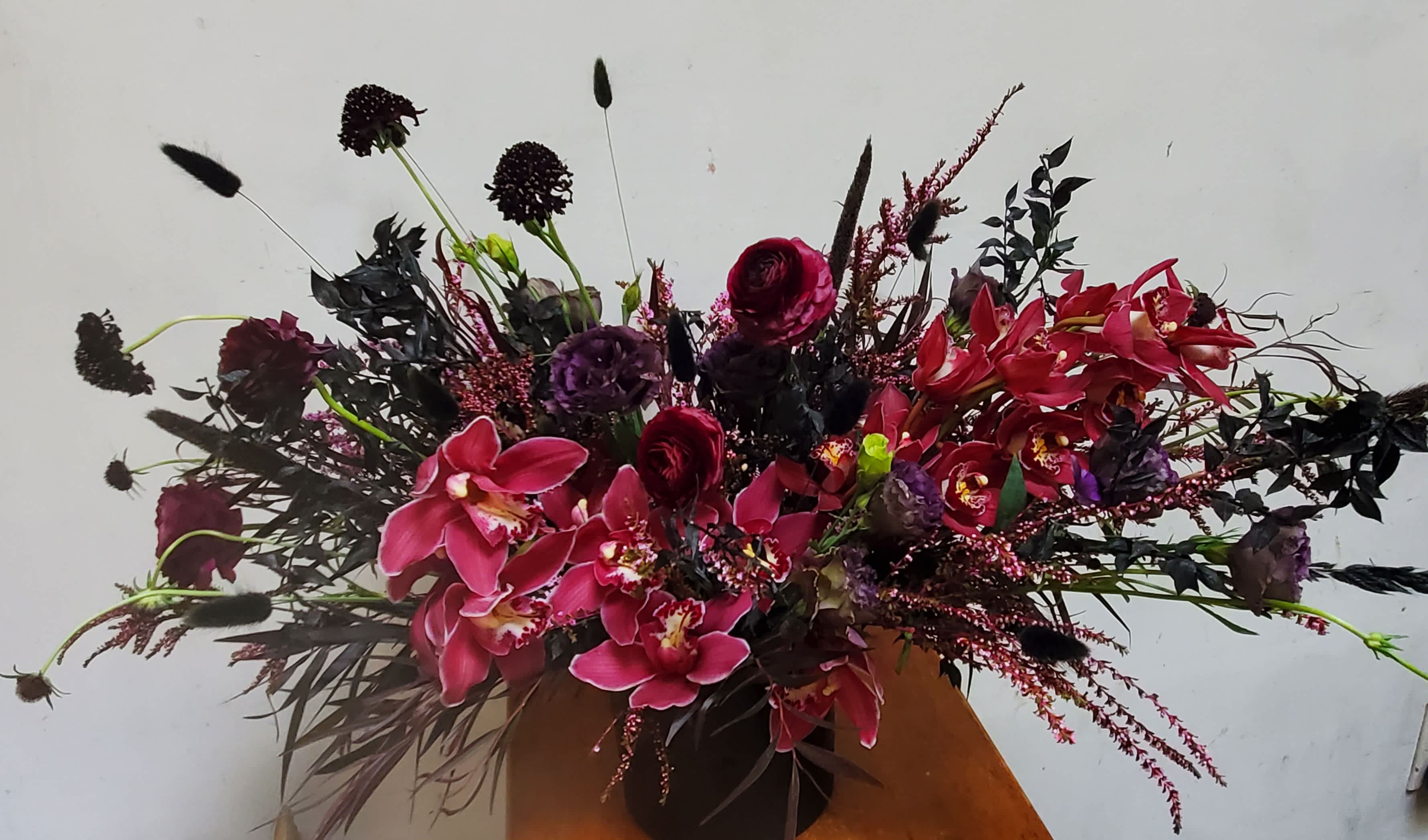 Large arrangement of pink orchids and dark red flowers in a vase