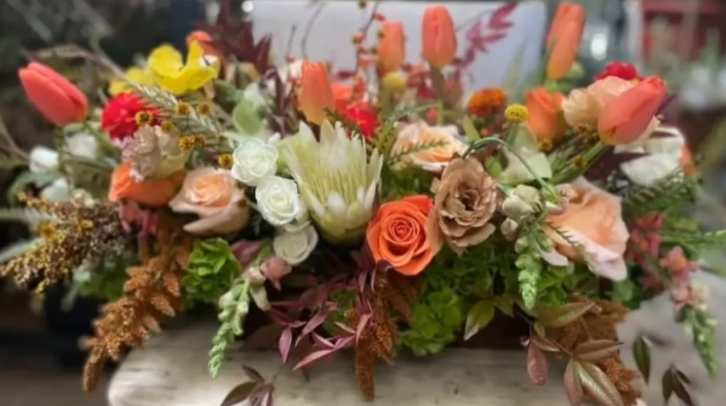Low floral arrangement with peach, coral, white, and yellow blooms