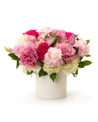 Low pink and white arrangement with roses, carnations, and orchids in a white cylinder vase