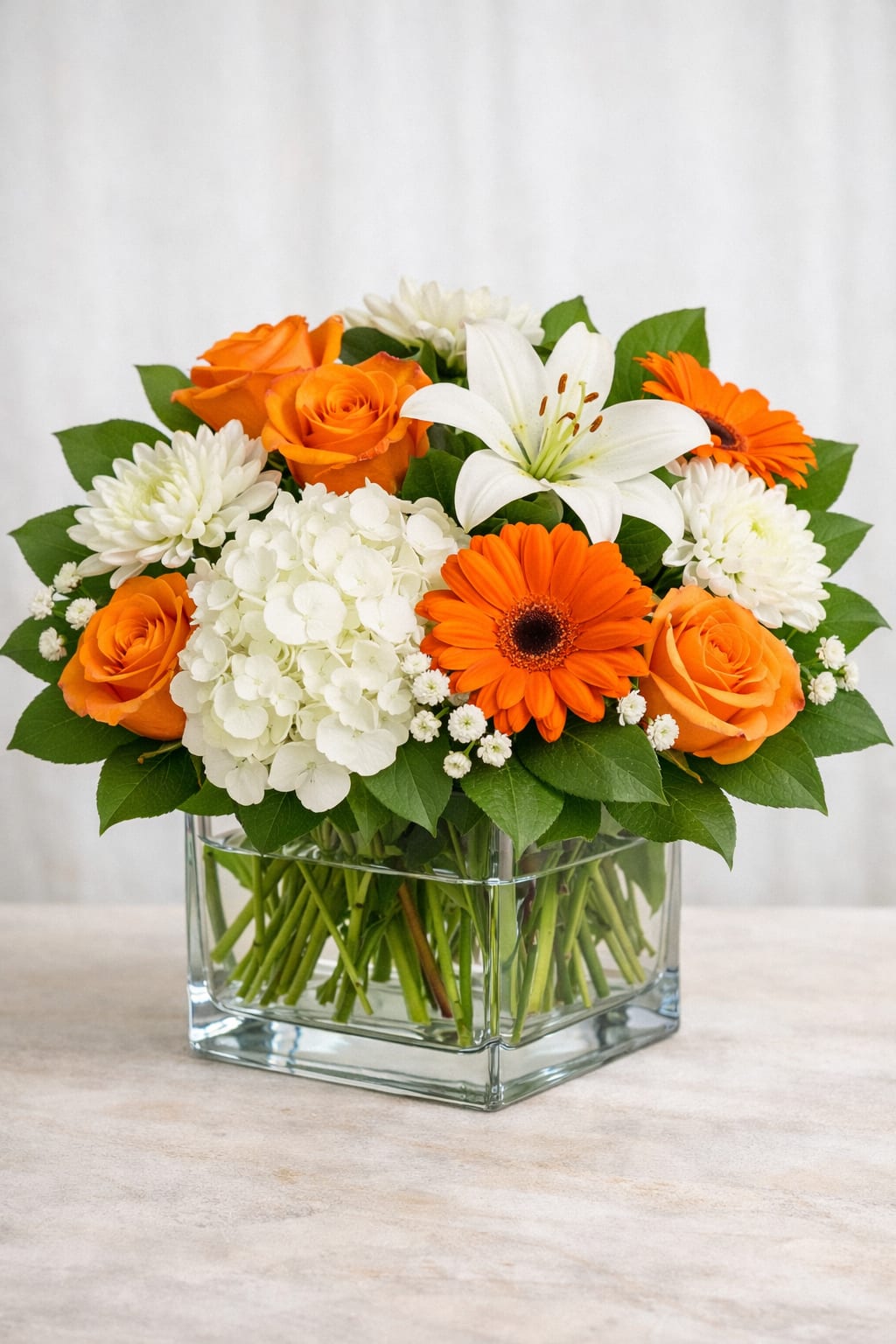 Radiant Honor - A bright mix of orange and white blooms with lush salal greenery in a clear glass cube, perfect for celebrating success.