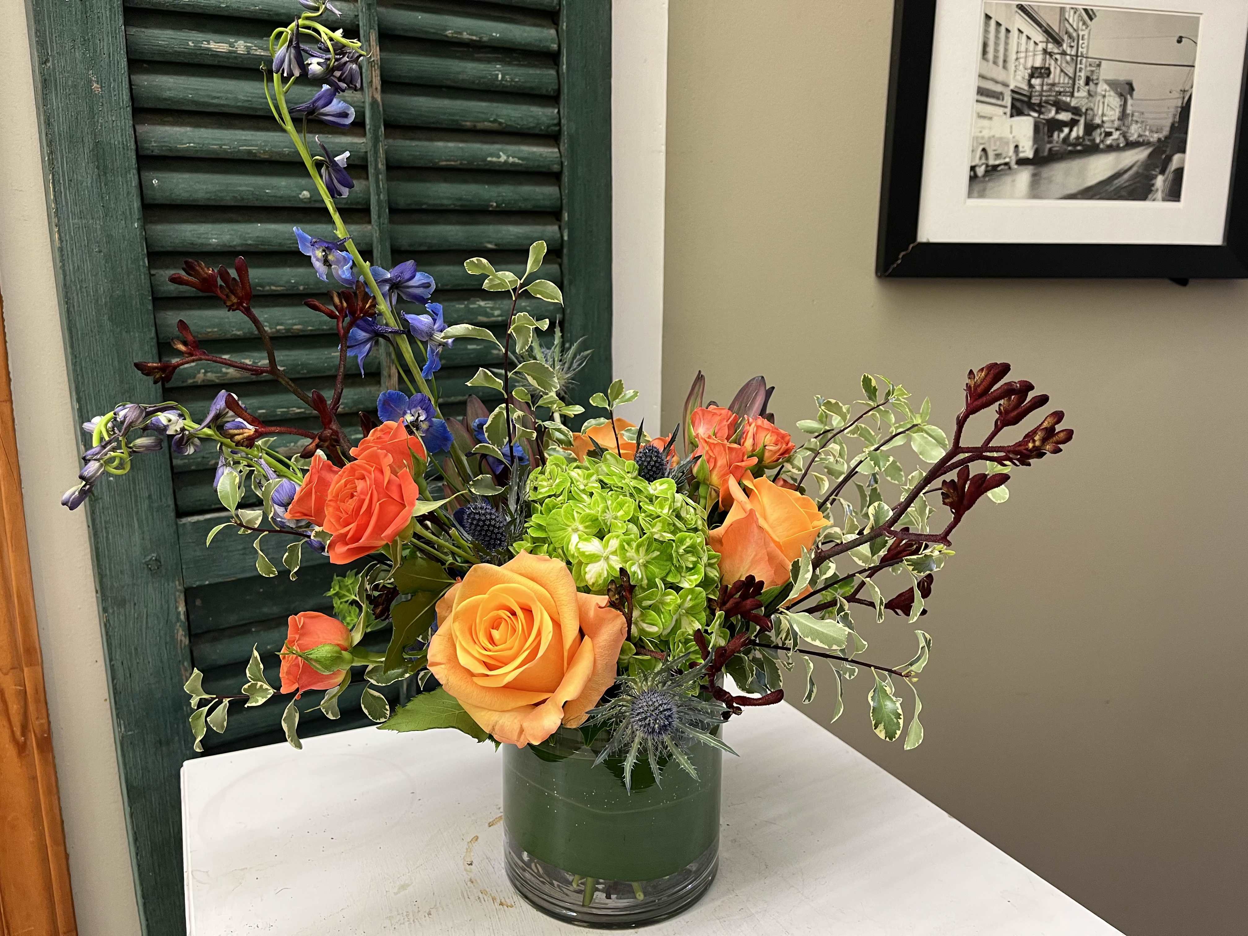 Orange and coral roses in a glass vase with blue flowers