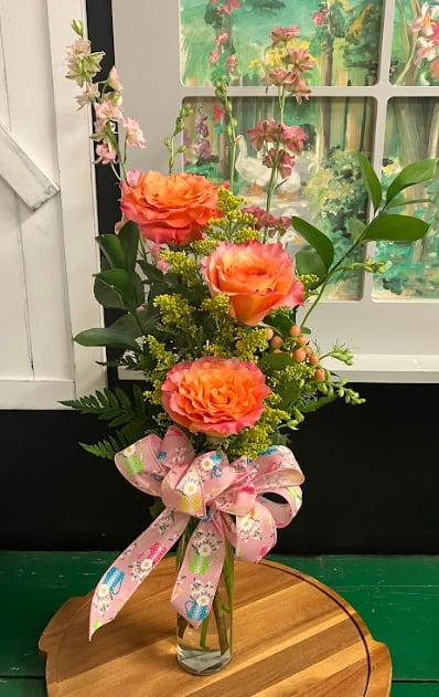 Tall bouquet of orange roses in a clear glass vase with a pink ribbon