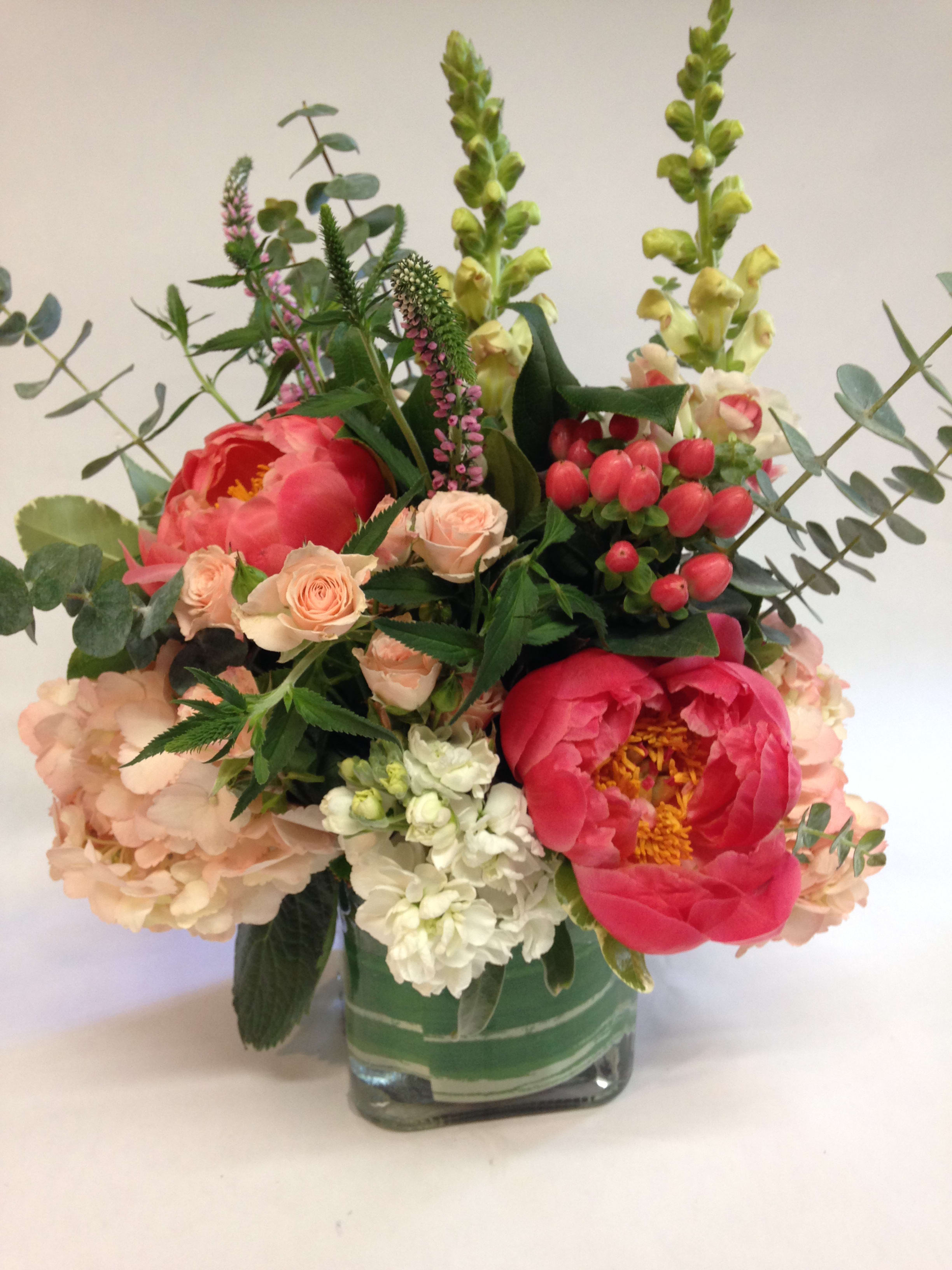 Mixed bouquet in a square glass vase with pink peonies and peach roses