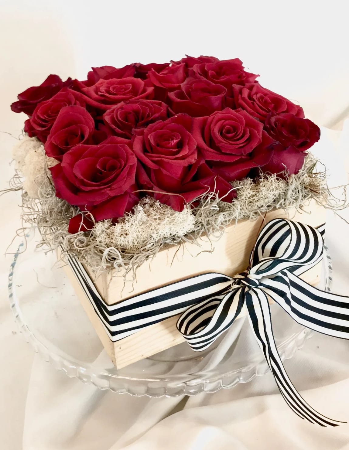 Red roses arranged in a square box with a striped ribbon bow