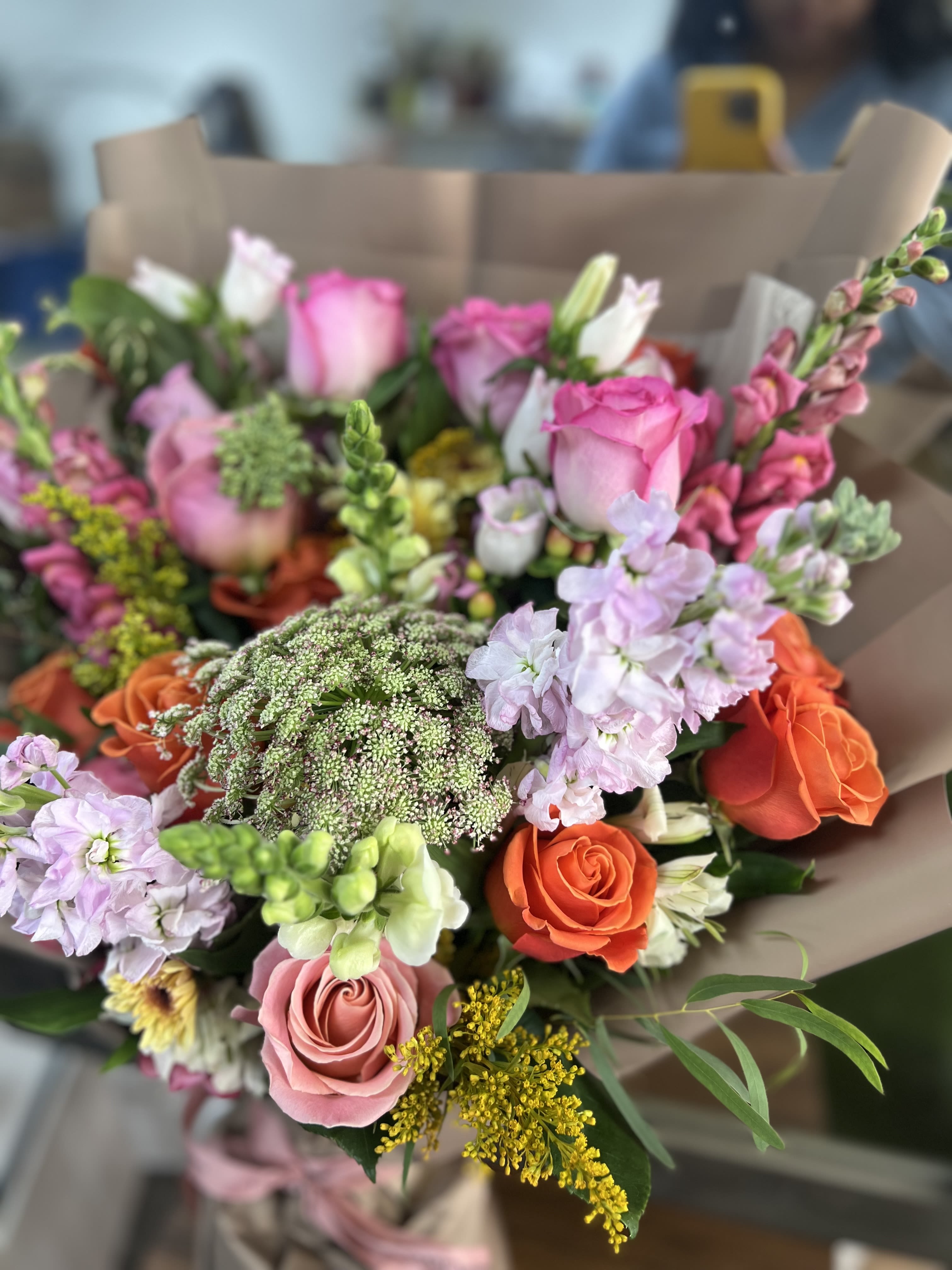 Mixed bouquet of pink, orange, and lavender flowers wrapped in brown paper