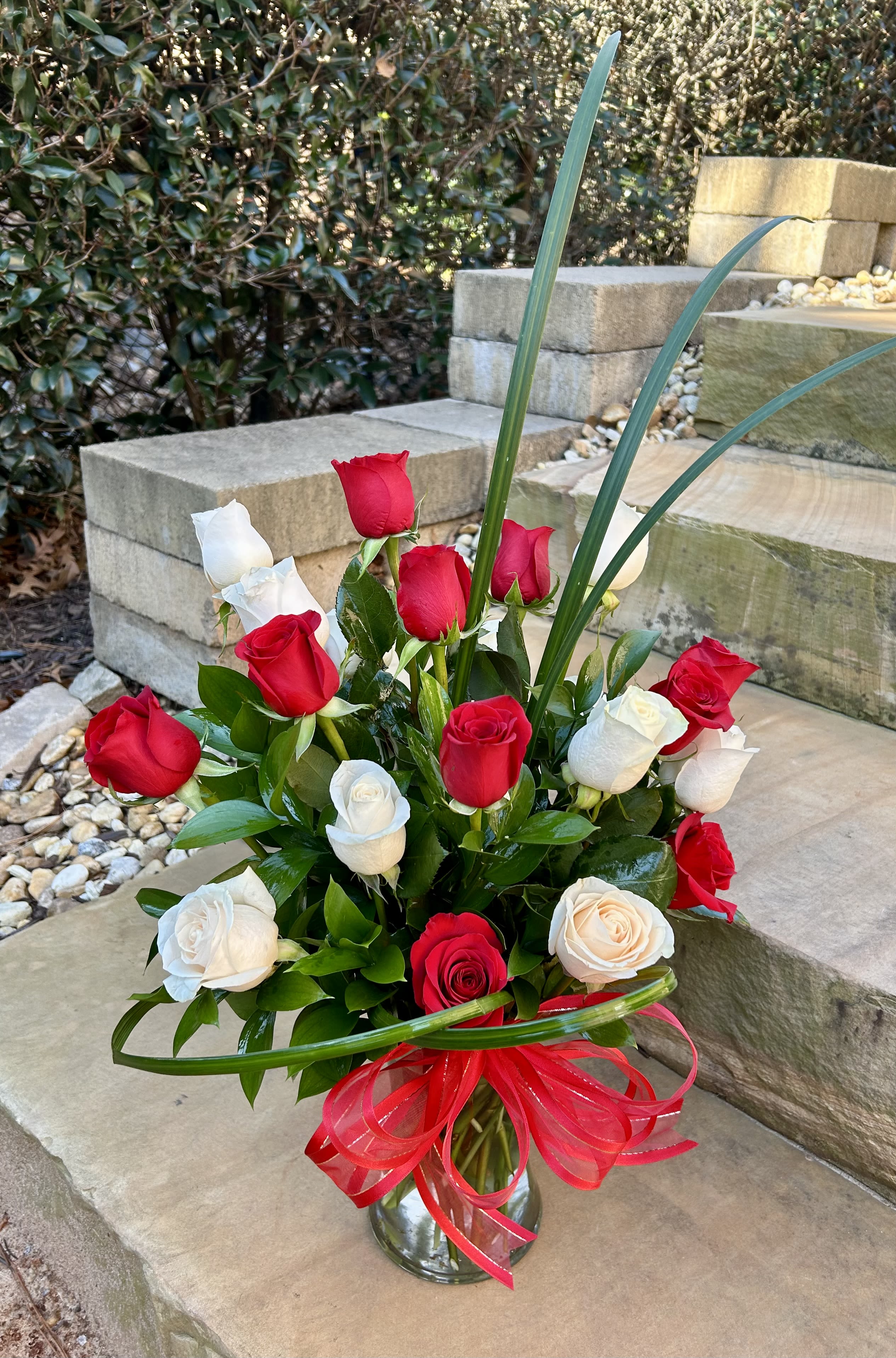 Red and white roses in a glass vase with a red ribbon
