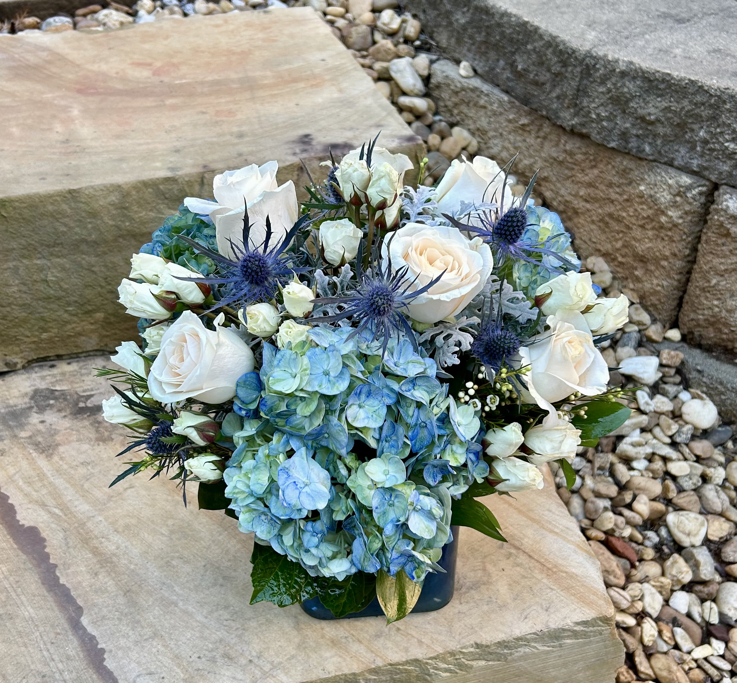 Blue hydrangeas and white roses arranged in a low square vase