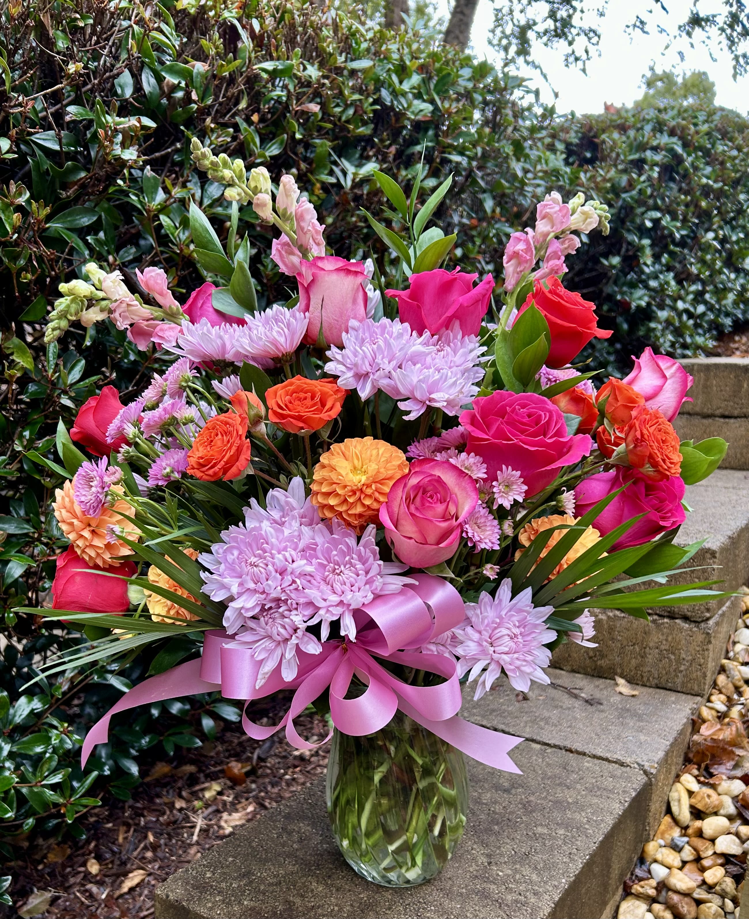 Pink and orange mixed flower bouquet in a glass vase with a pink ribbon