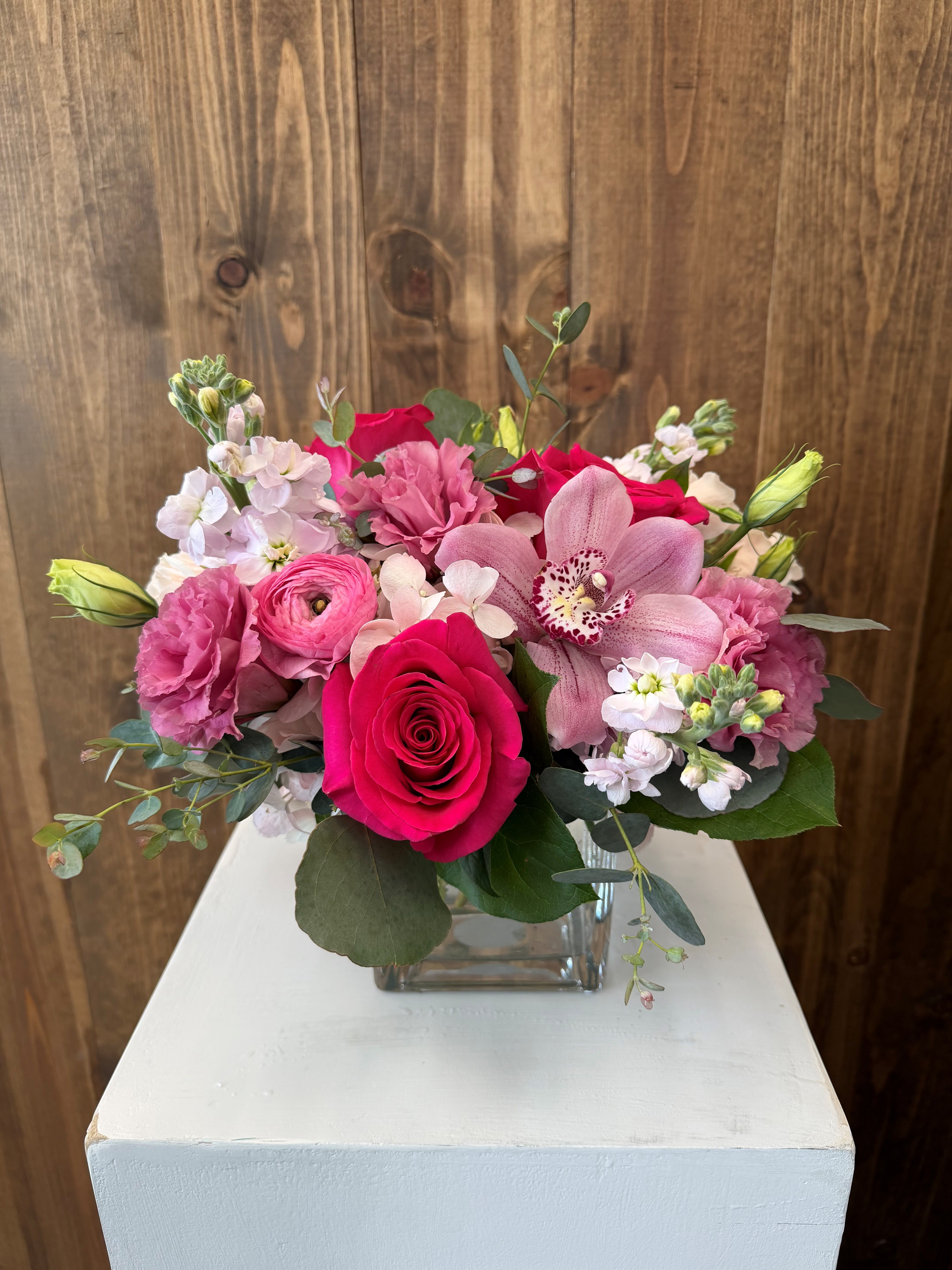 Pink and white bouquet with roses and orchids in a square glass vase