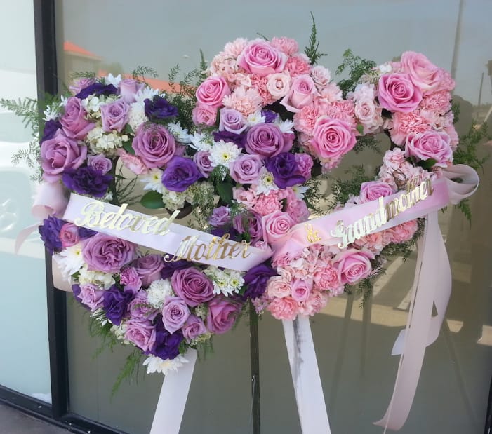 Heart-shaped floral tribute with pink and purple roses and ribbons