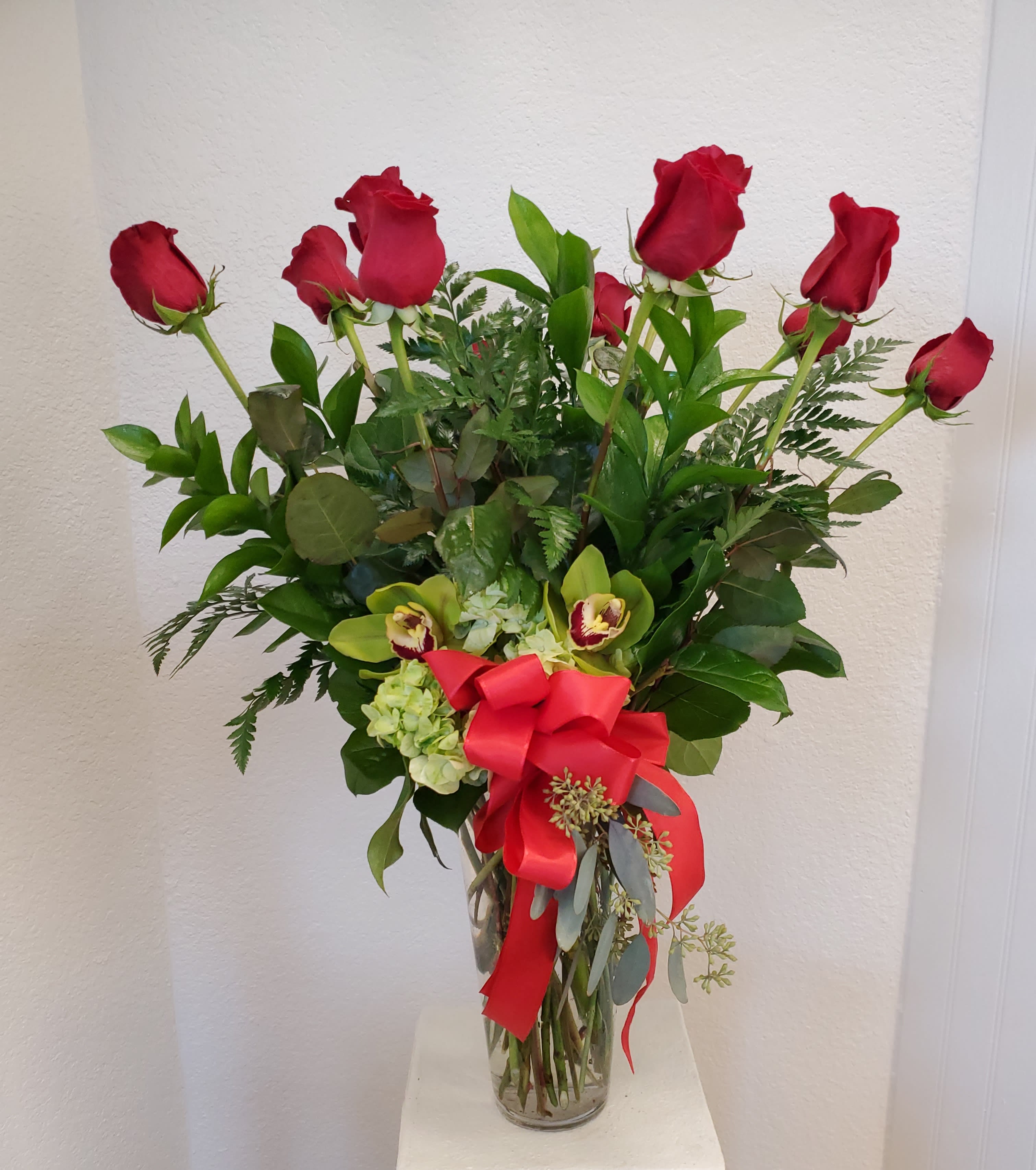 Red roses and green orchids in a glass vase with a red ribbon