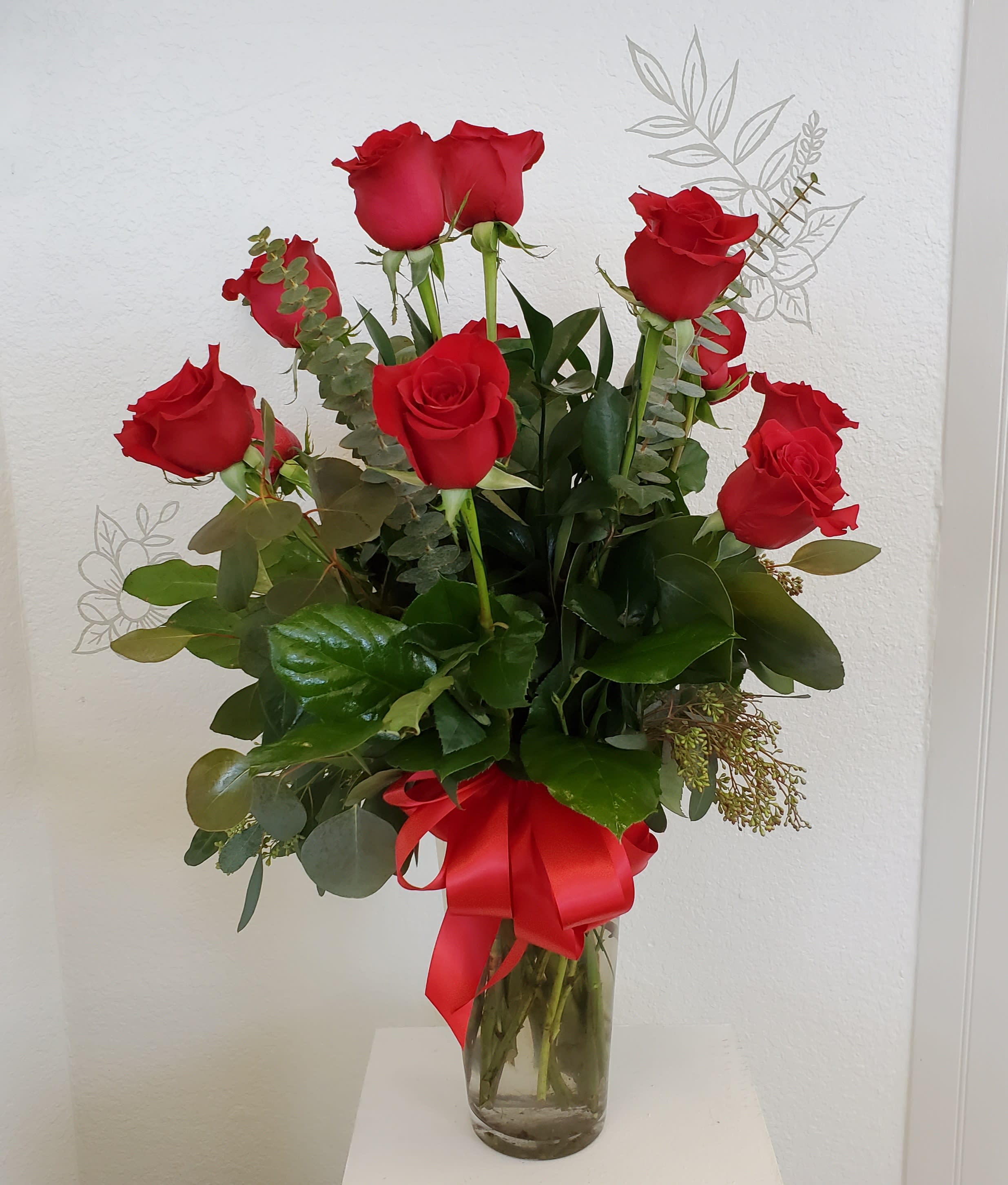 Red roses arranged in a clear glass vase with a red ribbon.