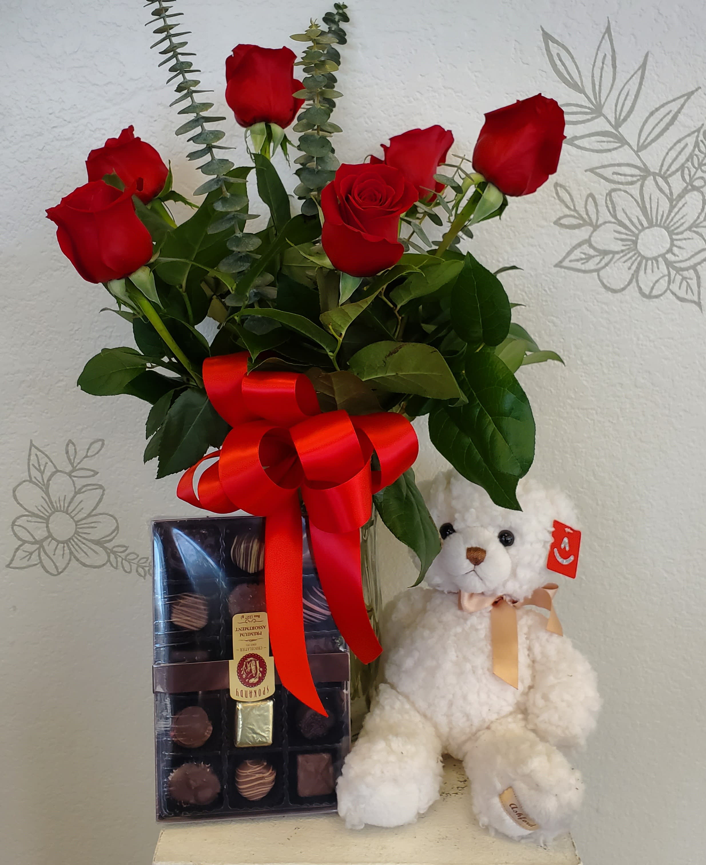 Red roses in a glass vase with a teddy bear and chocolate box