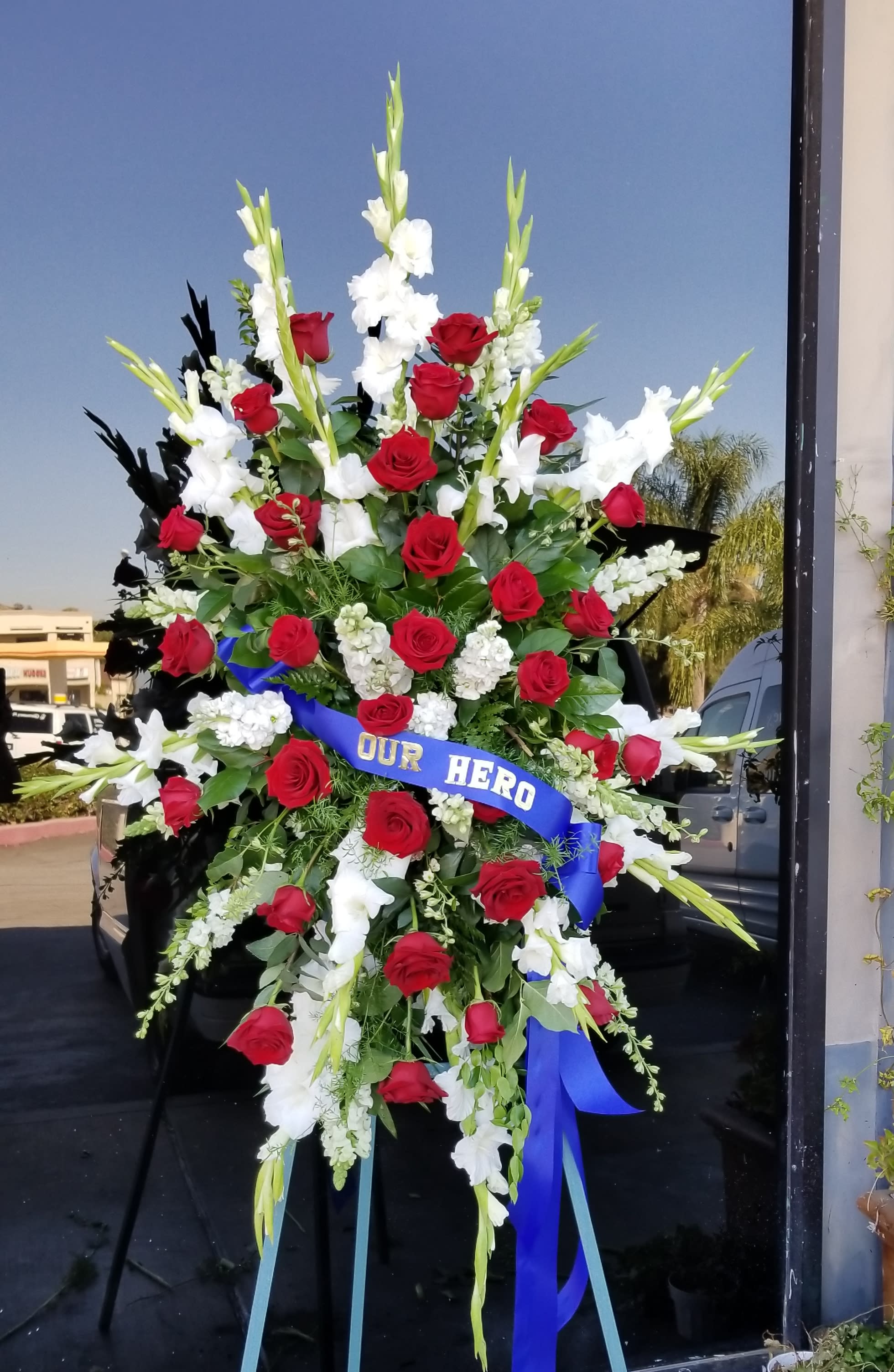 Large standing spray of red roses and white gladiolus with a blue ribbon