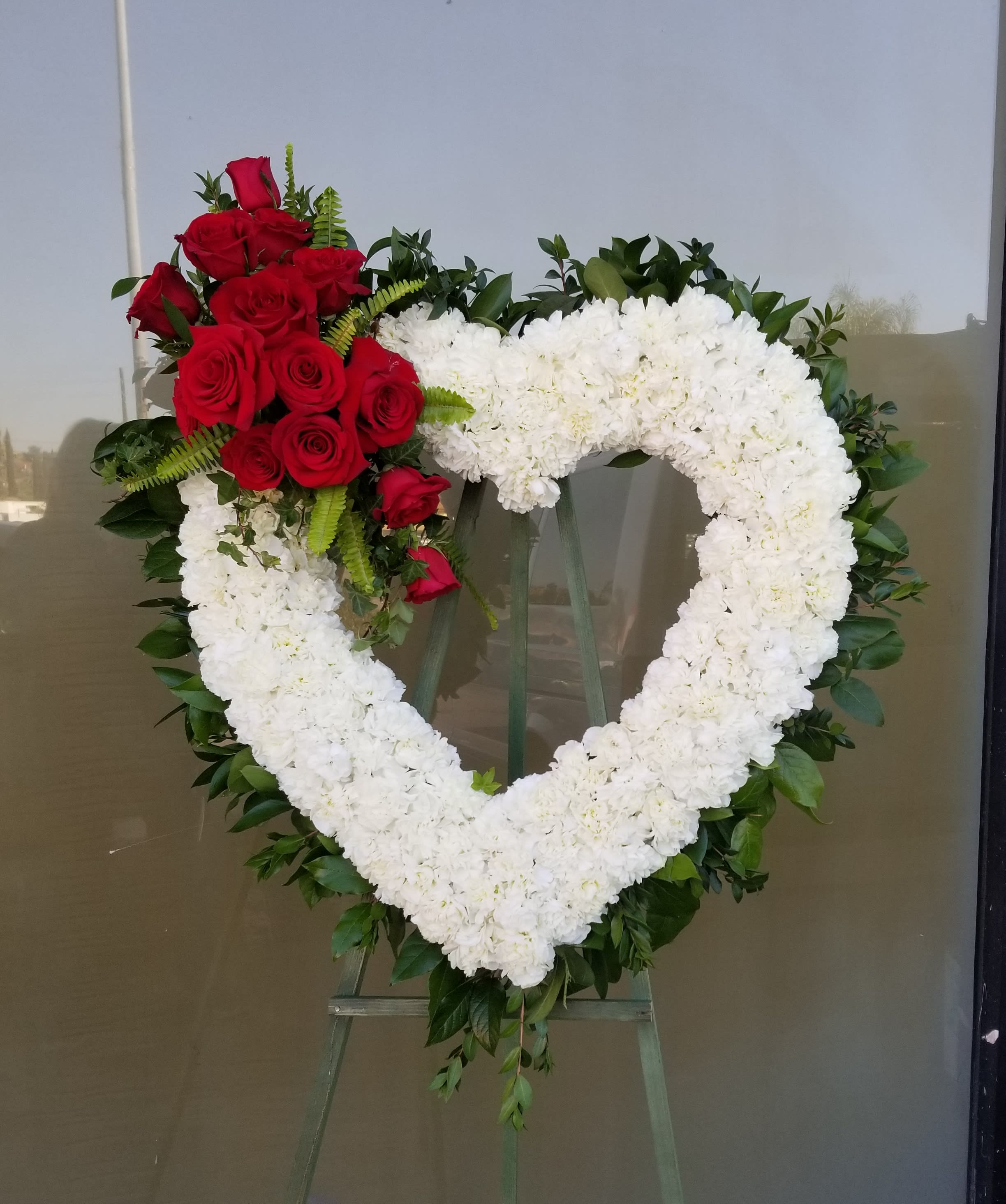 Heart-shaped floral wreath with white blooms and red roses on an easel