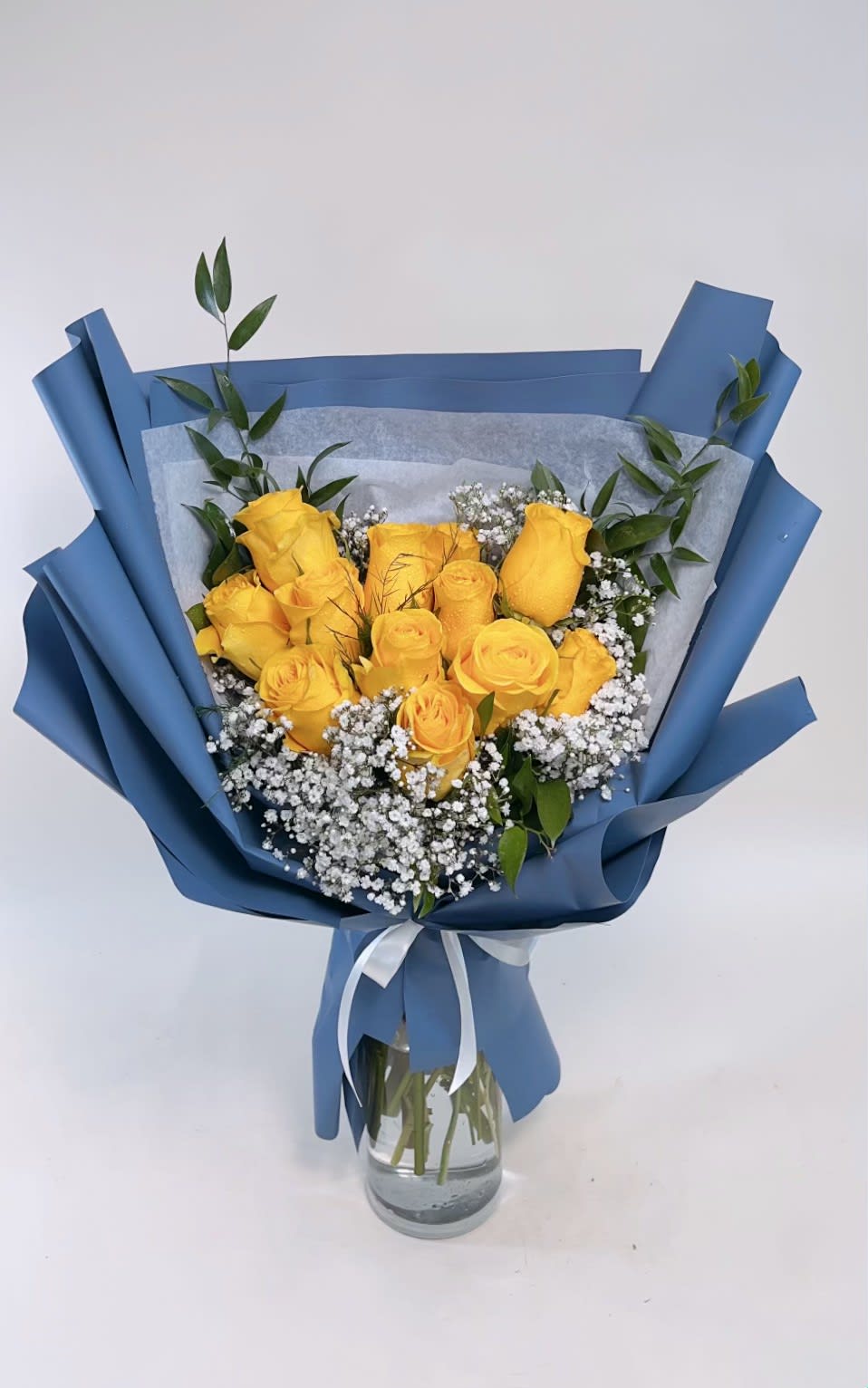 Yellow roses in blue wrapping with baby's breath in a glass vase