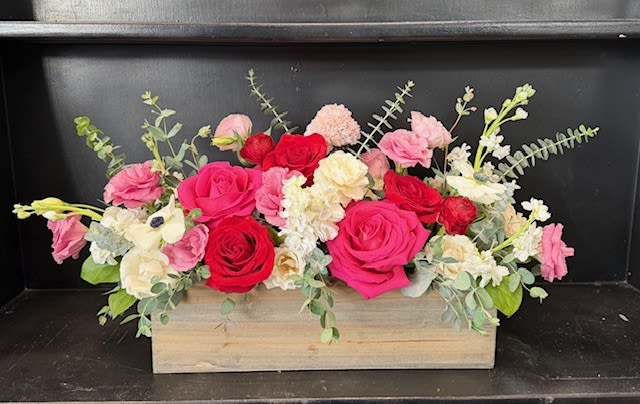 Pink and red roses arranged in a wooden box with white flowers