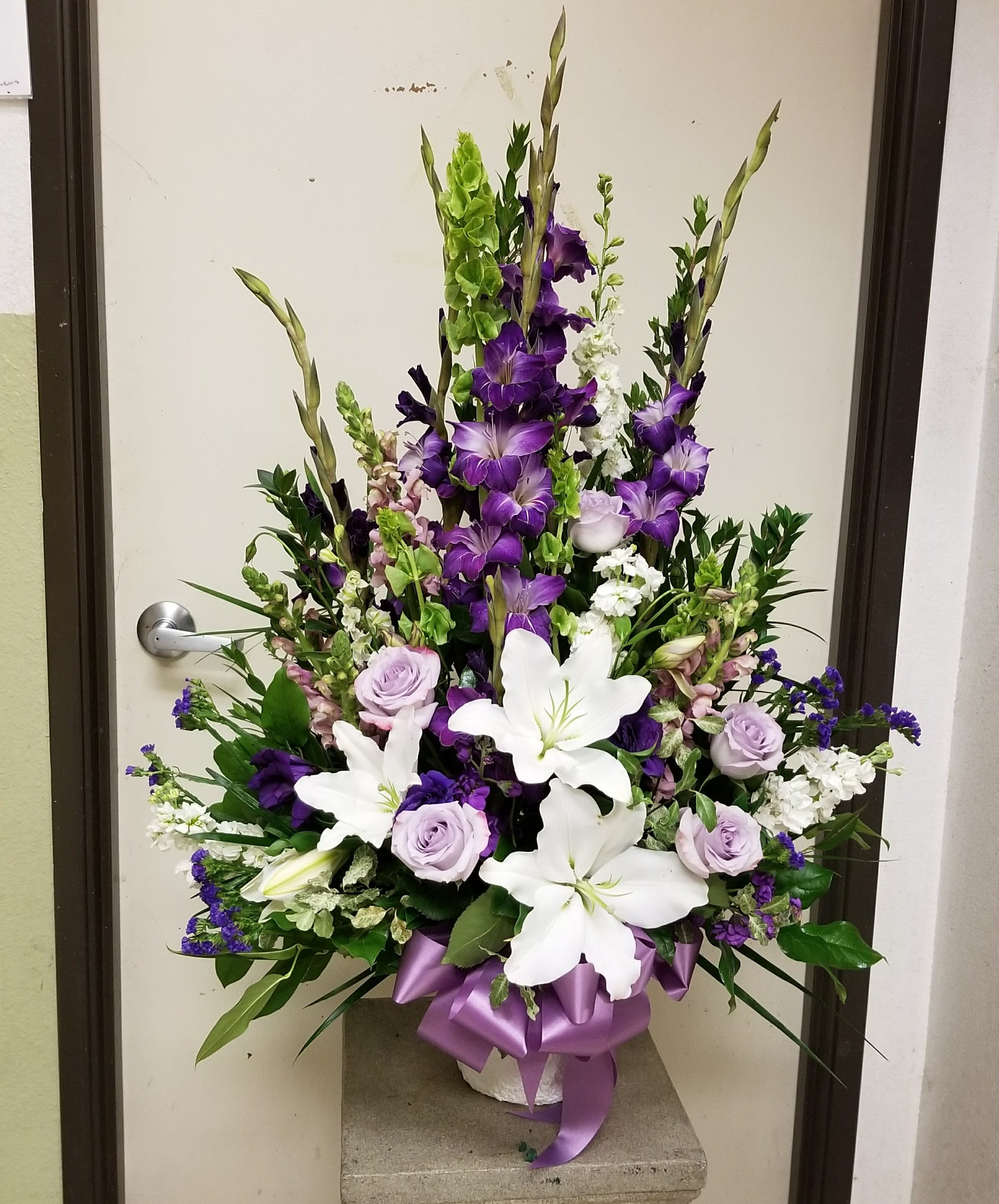 Tall floral arrangement with white lilies, purple roses, and purple spikes in a vase