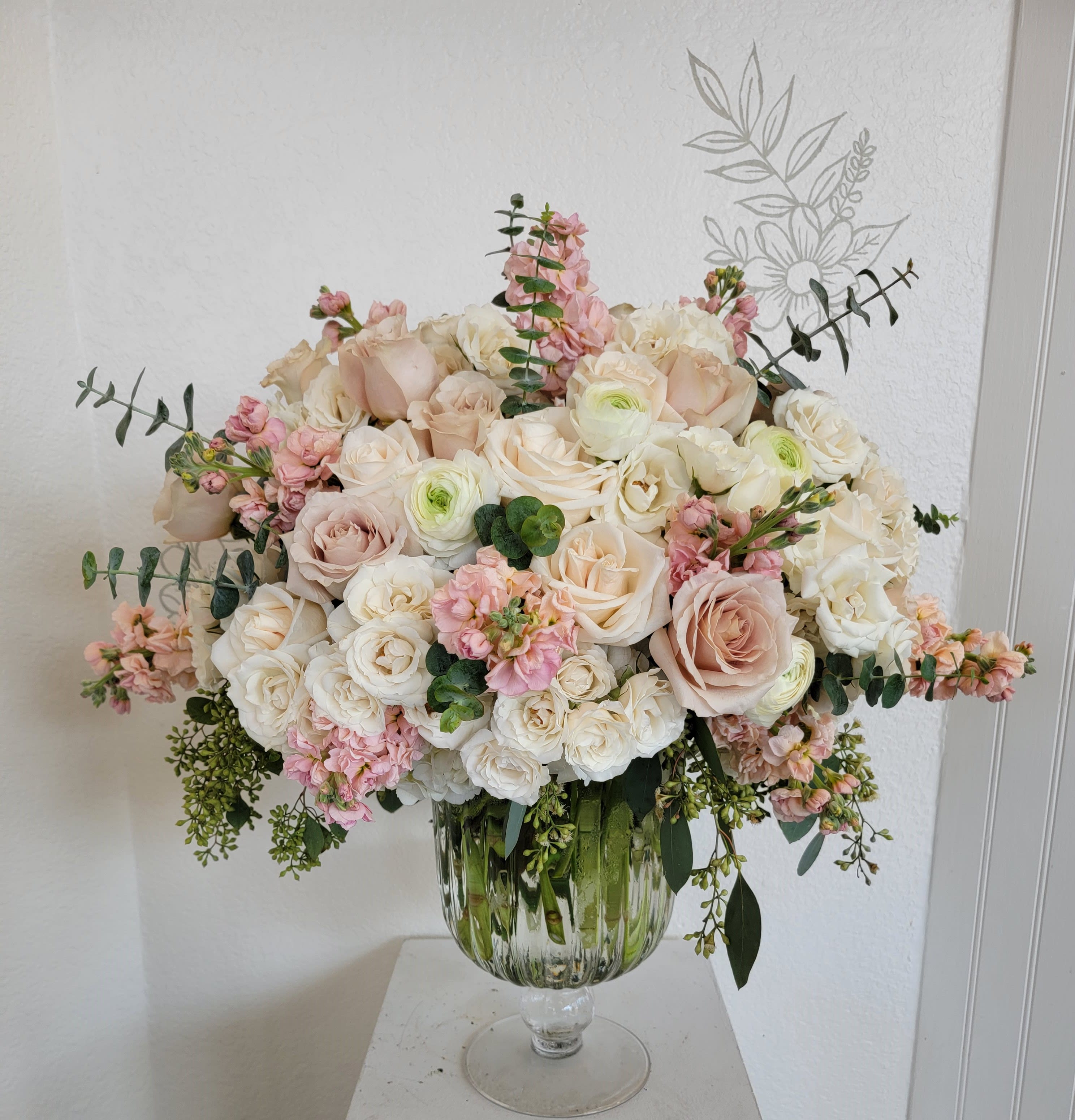 Large blush and white rose arrangement in a glass pedestal vase