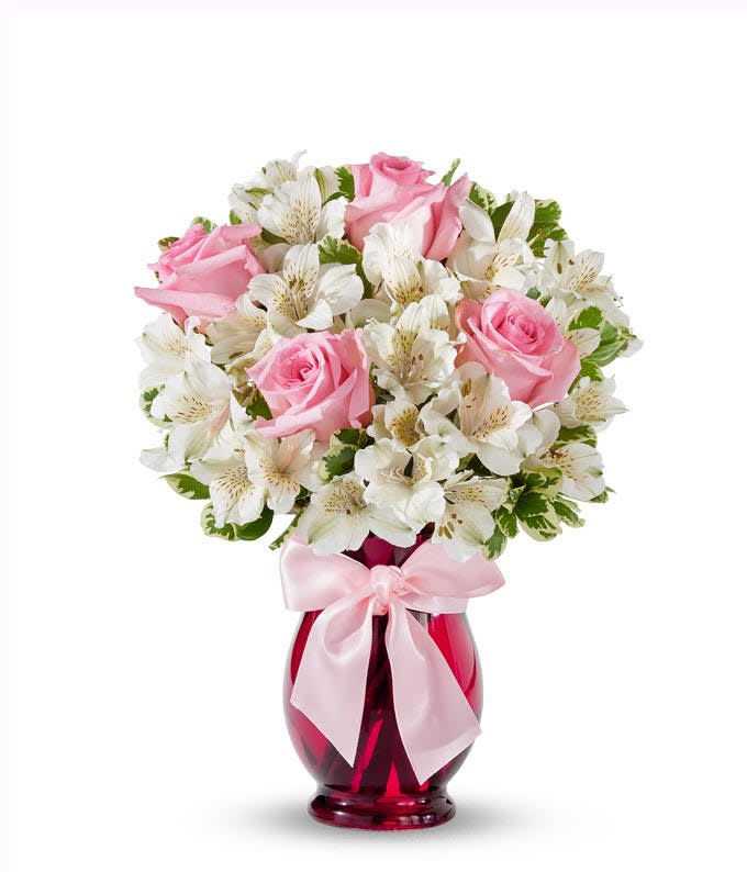 Pink roses and white flowers in a red glass vase with a pink ribbon