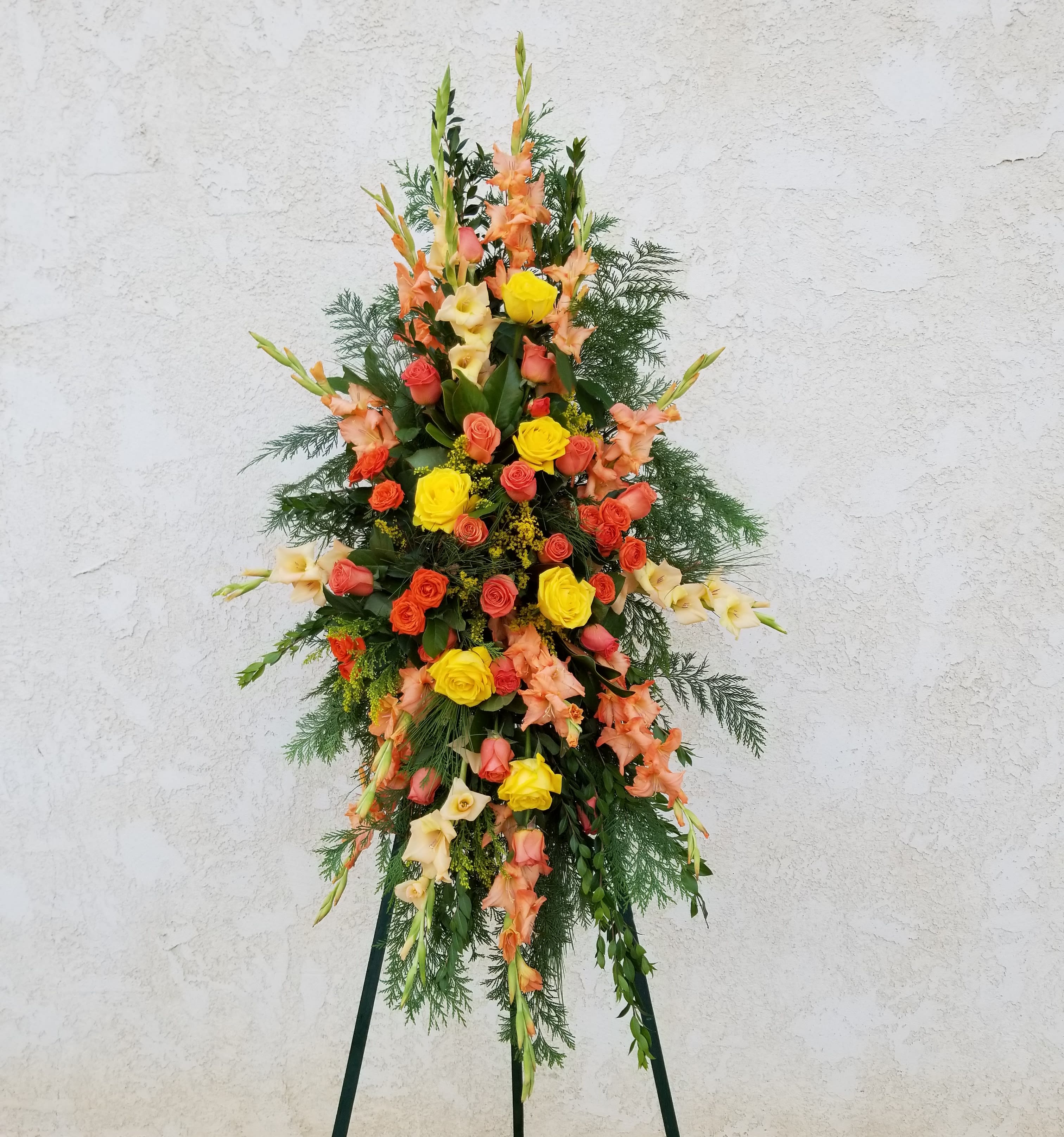 Tall standing floral spray with roses and gladiolus in orange, yellow, and cream