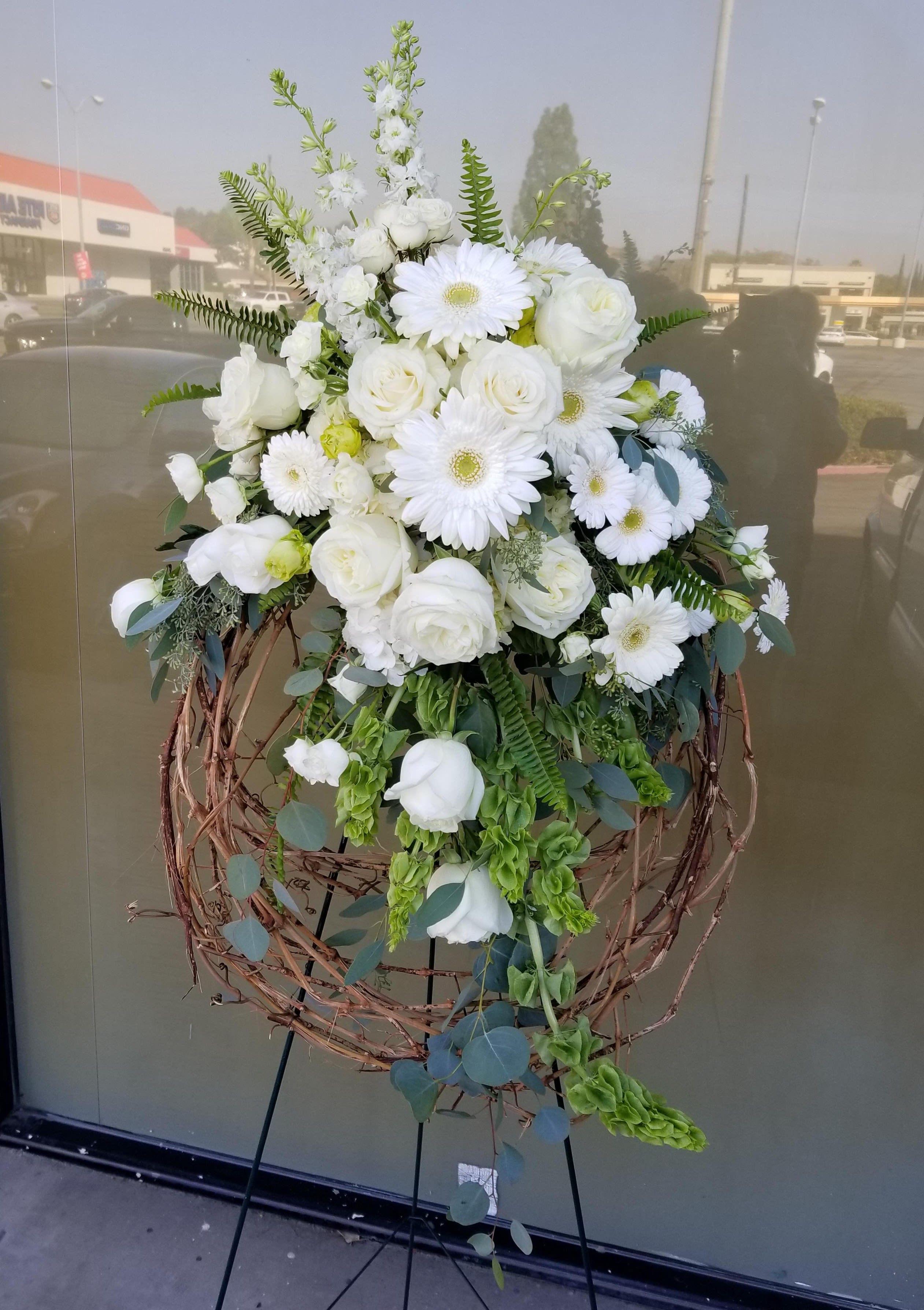 White floral standing arrangement with roses and daisies on a twig wreath stand
