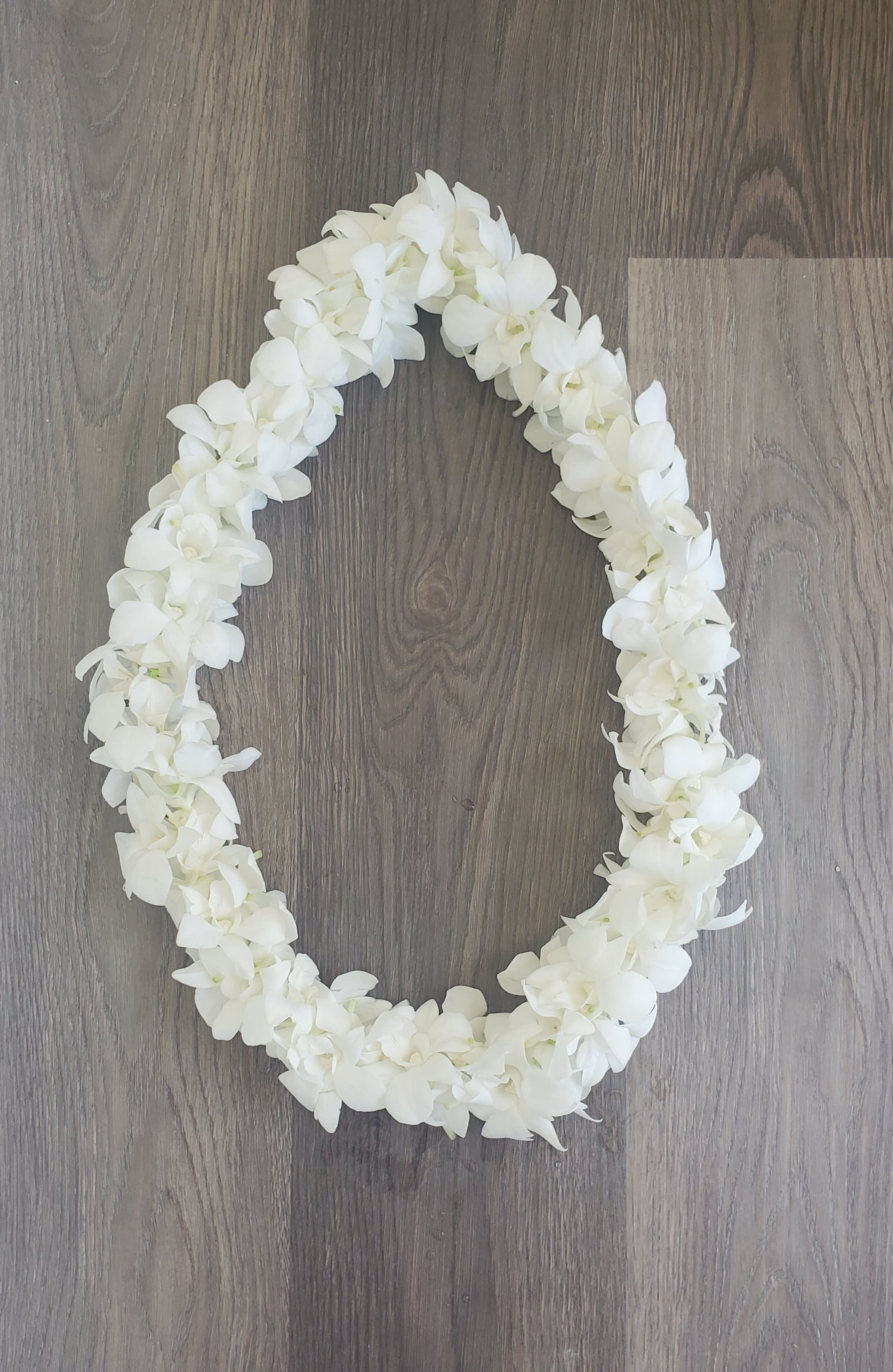White floral lei arranged in an oval shape on a wood floor