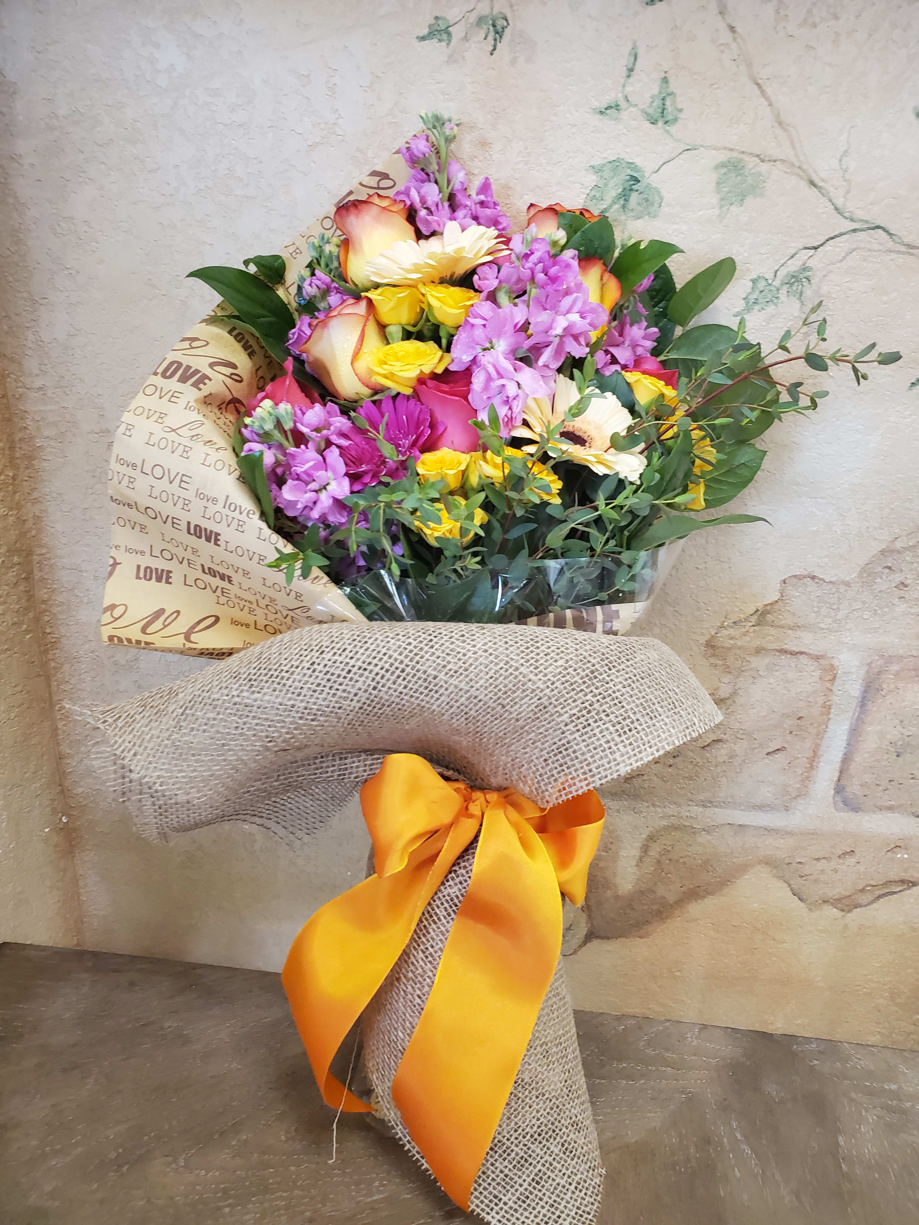 Mixed bouquet of roses, daisies, and purple flowers wrapped with burlap and ribbon