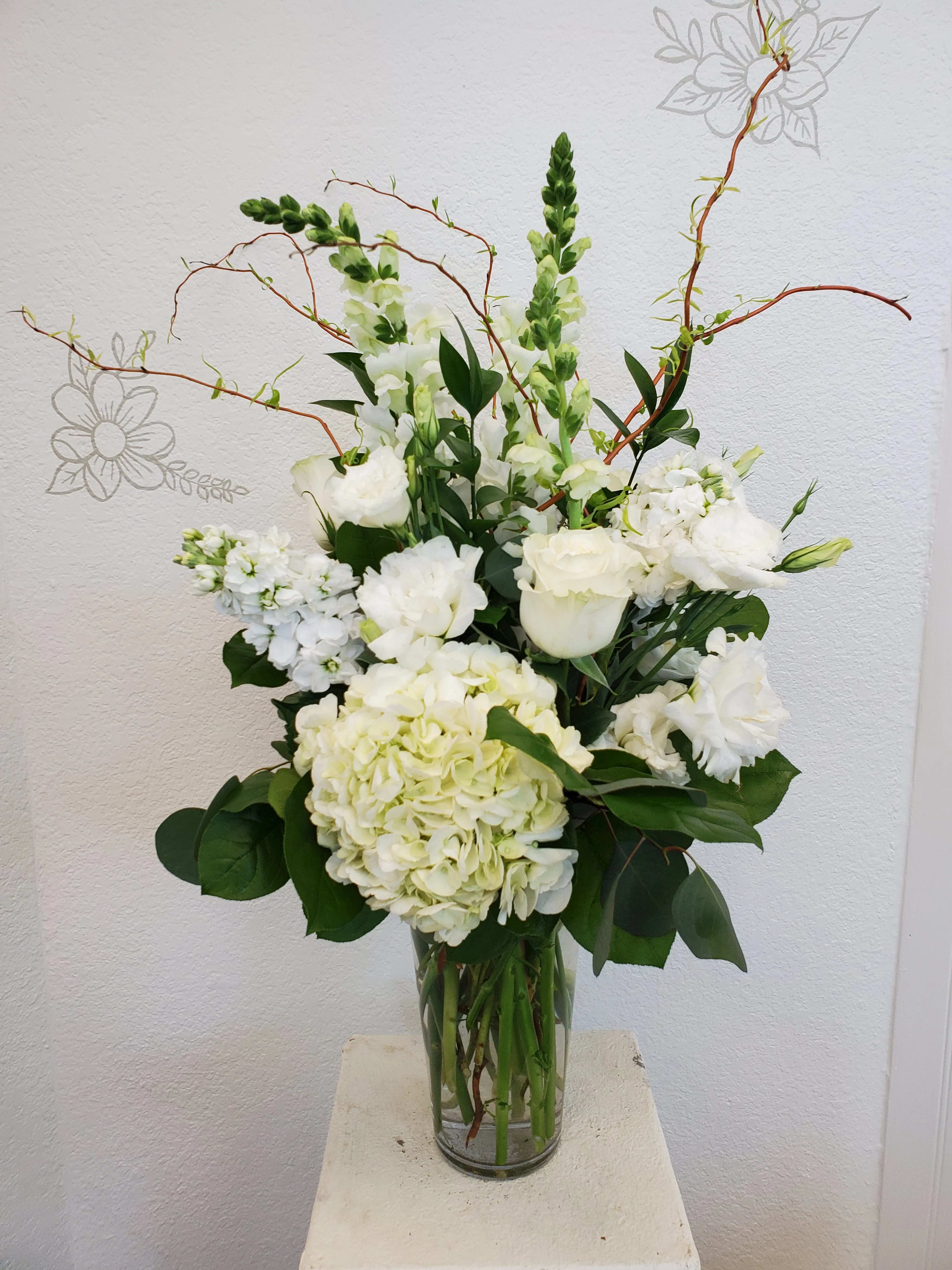White floral arrangement in a clear glass vase with tall branching stems