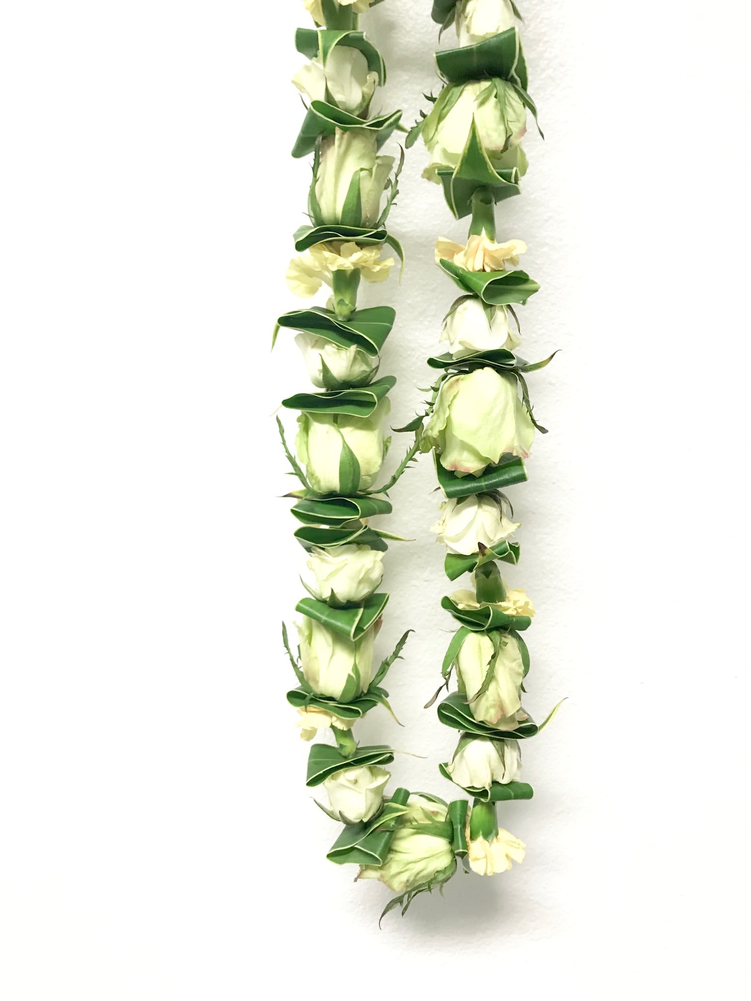 Two white rose leis with green accents on a white background