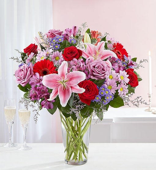 Mixed bouquet of roses, lilies, and daisies in a clear glass vase