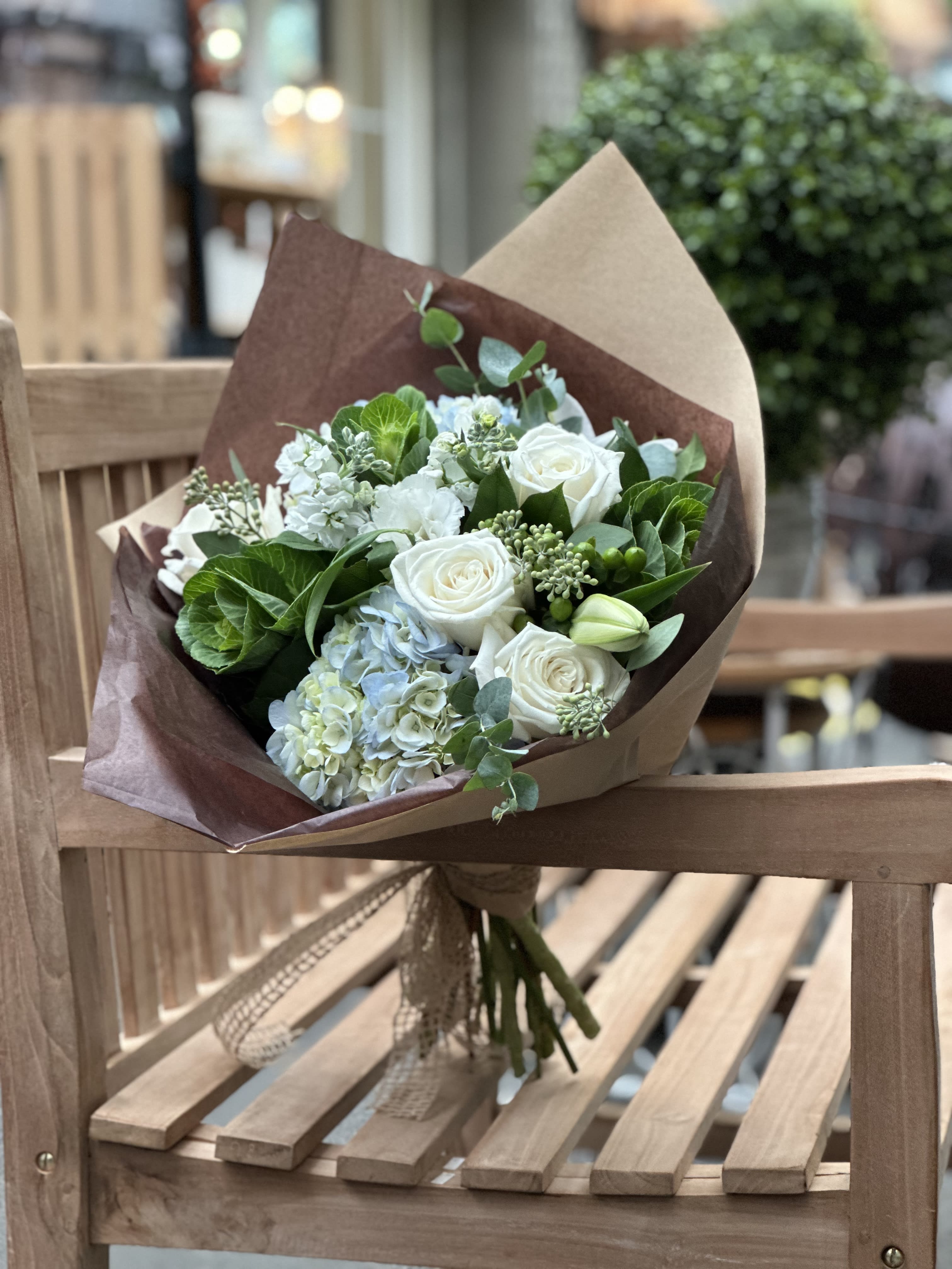 Bouquet of white roses and pale blue hydrangeas wrapped in brown paper