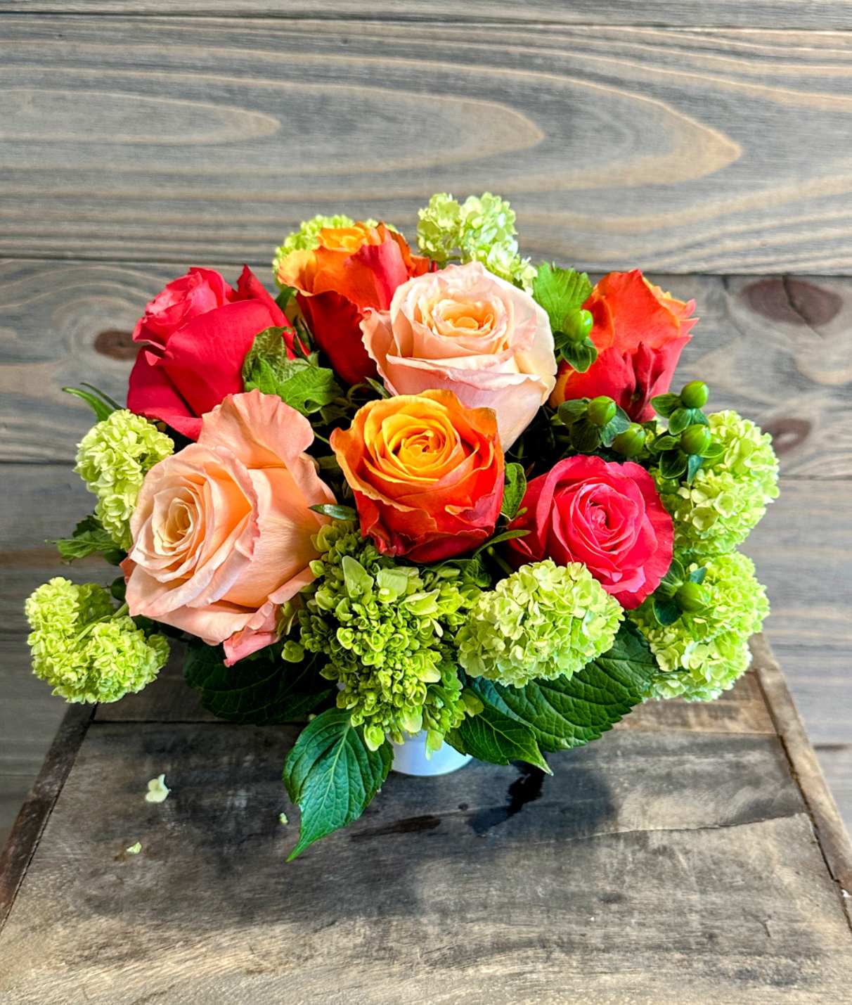 Coral Sunset - A small container of sunset toned roses with some spring greenery.