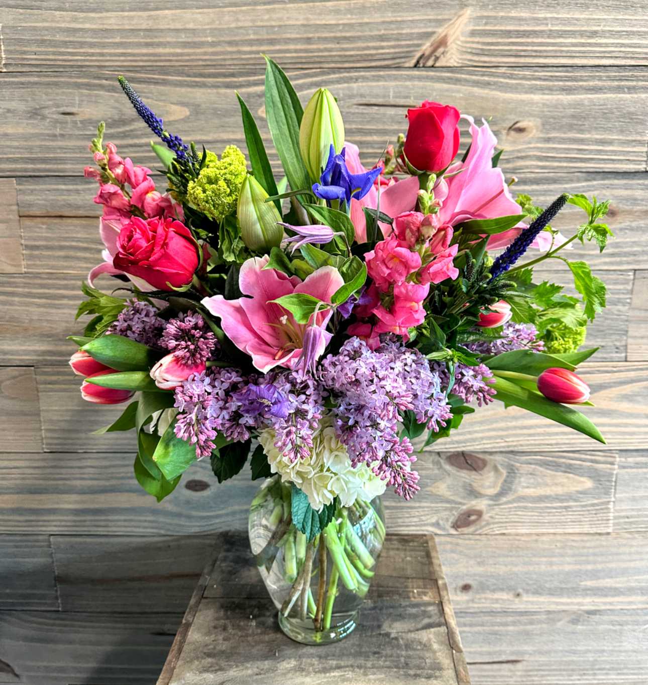 Mixed bouquet of pink, purple, and red flowers in a clear glass vase