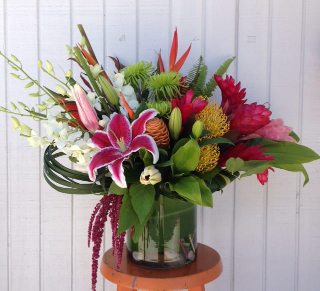 Tropical bouquet with pink lily, red blooms, and orchids in a glass vase