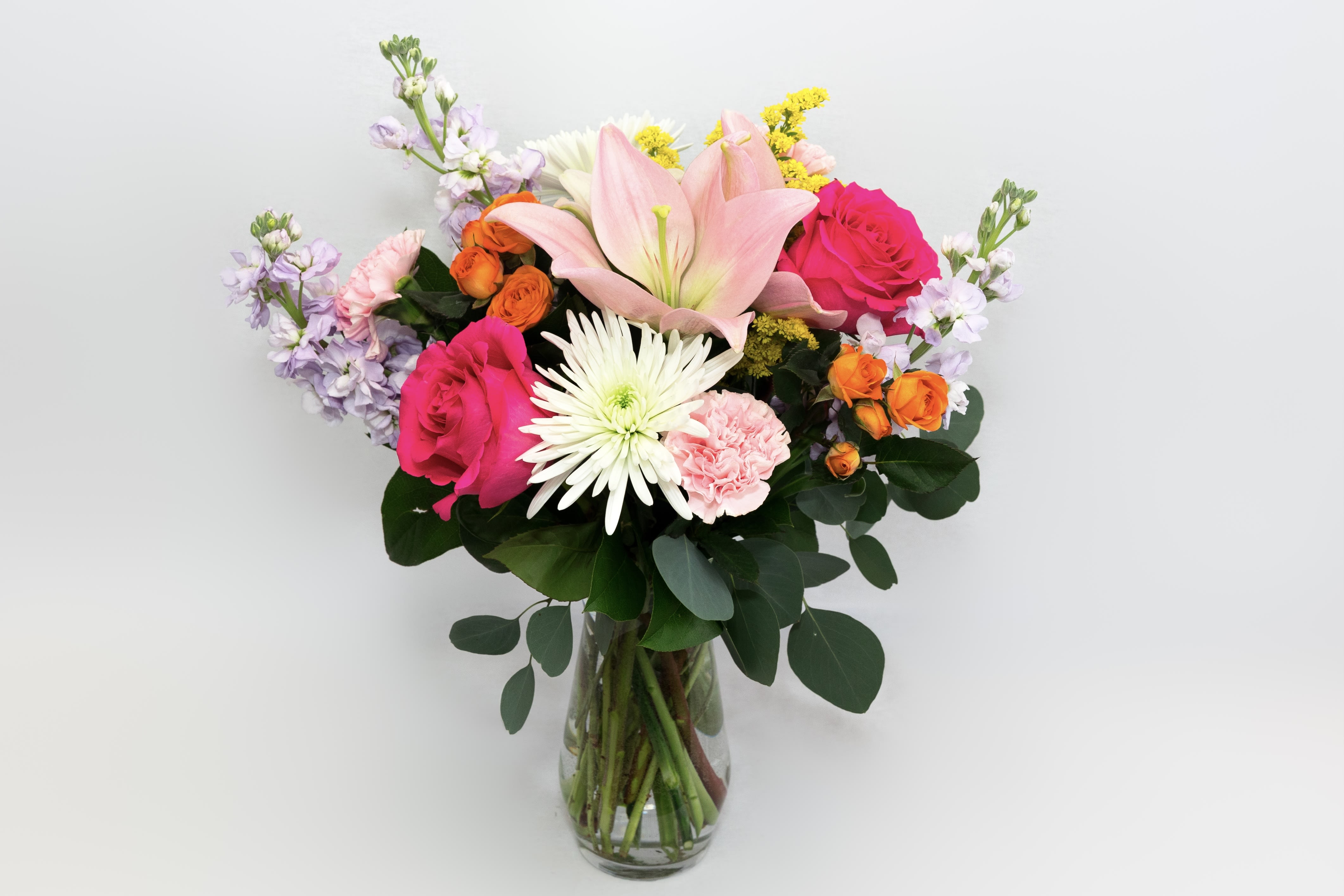 Mixed bouquet of pink, white, orange, and lavender flowers in a glass vase