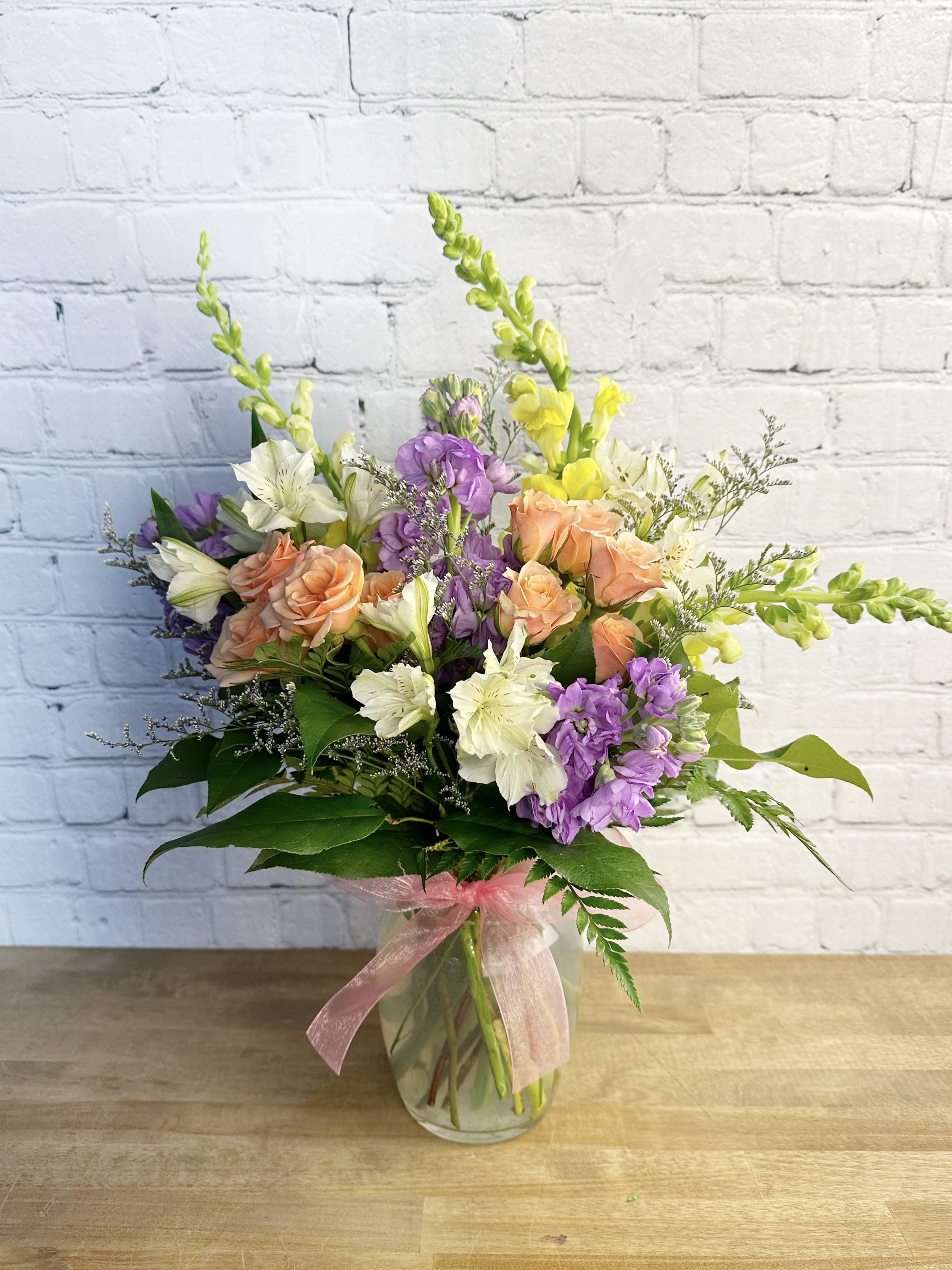Mixed bouquet of peach roses, purple flowers, and white blooms in a glass vase