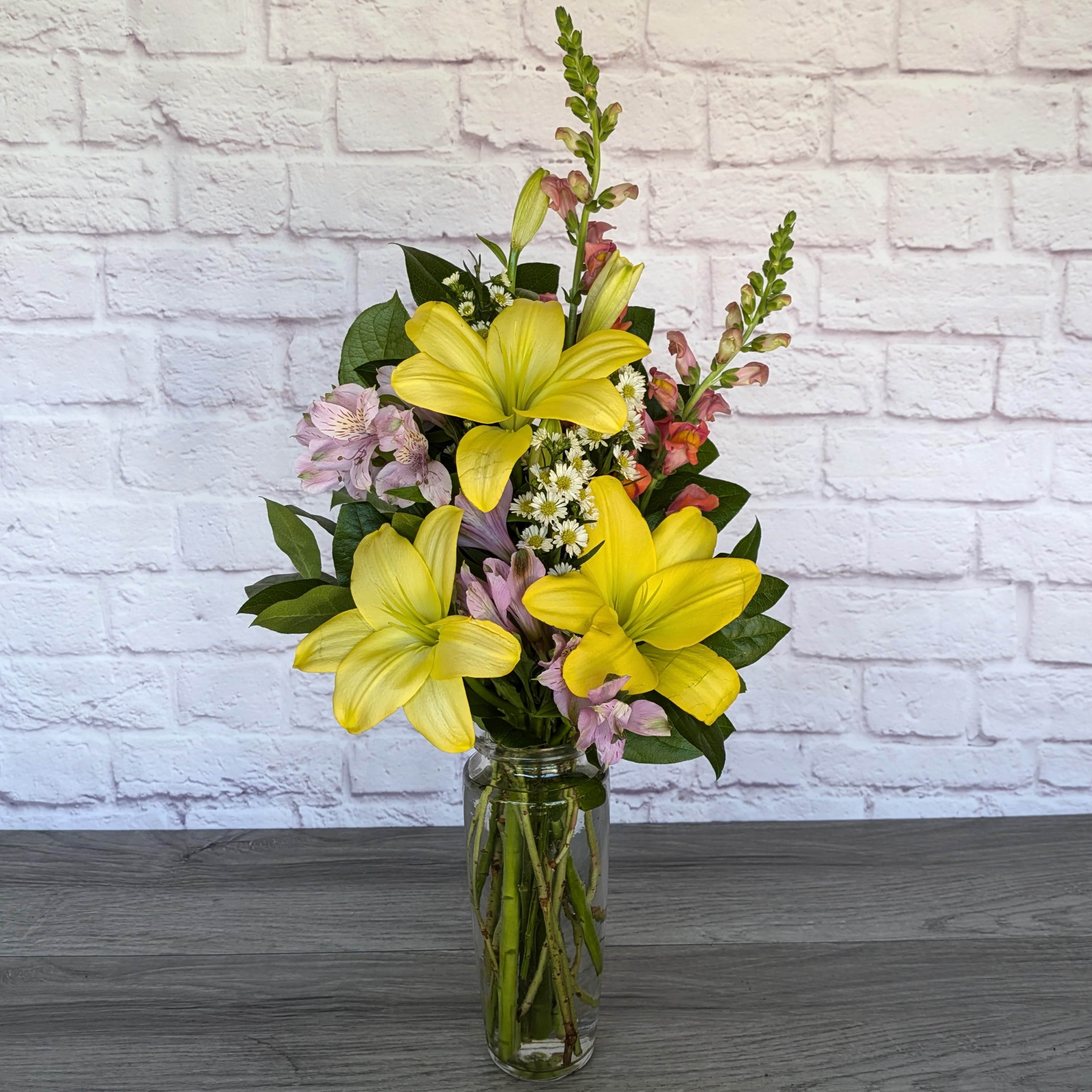 Yellow lilies and pink flowers arranged in a clear glass vase.