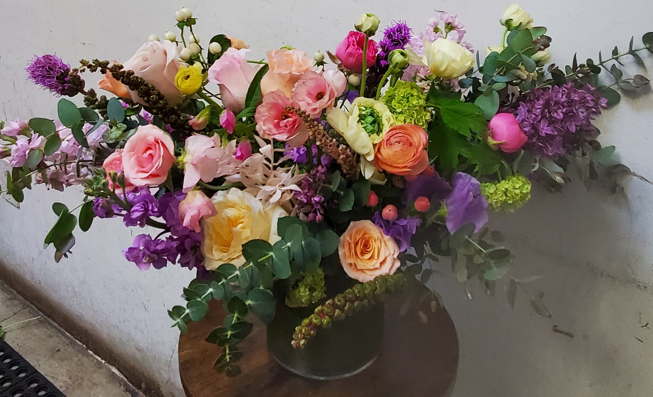 Large mixed bouquet of pink, peach, purple, and yellow flowers in a dark vase