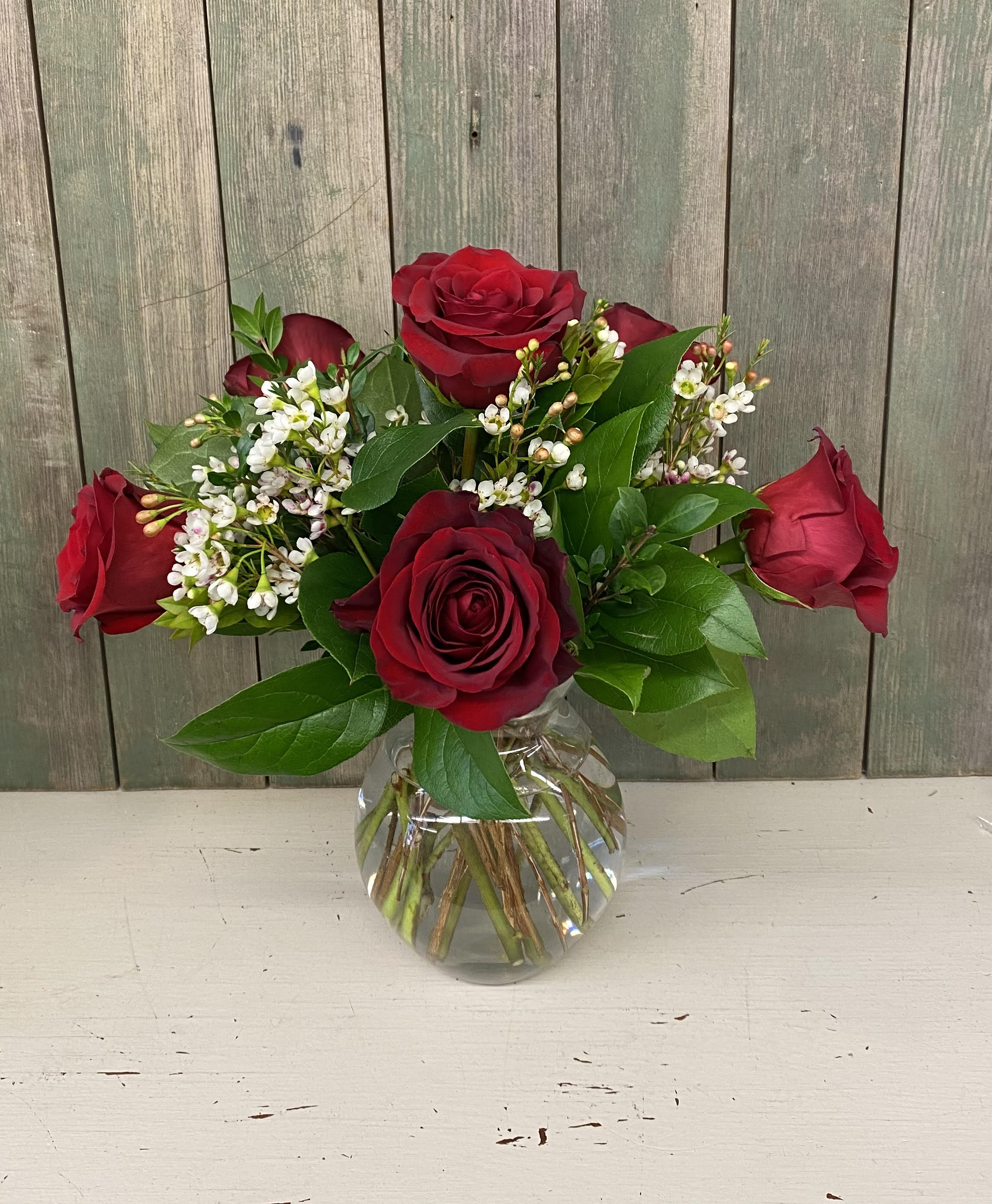 Red roses arranged in a clear glass vase with small white filler flowers