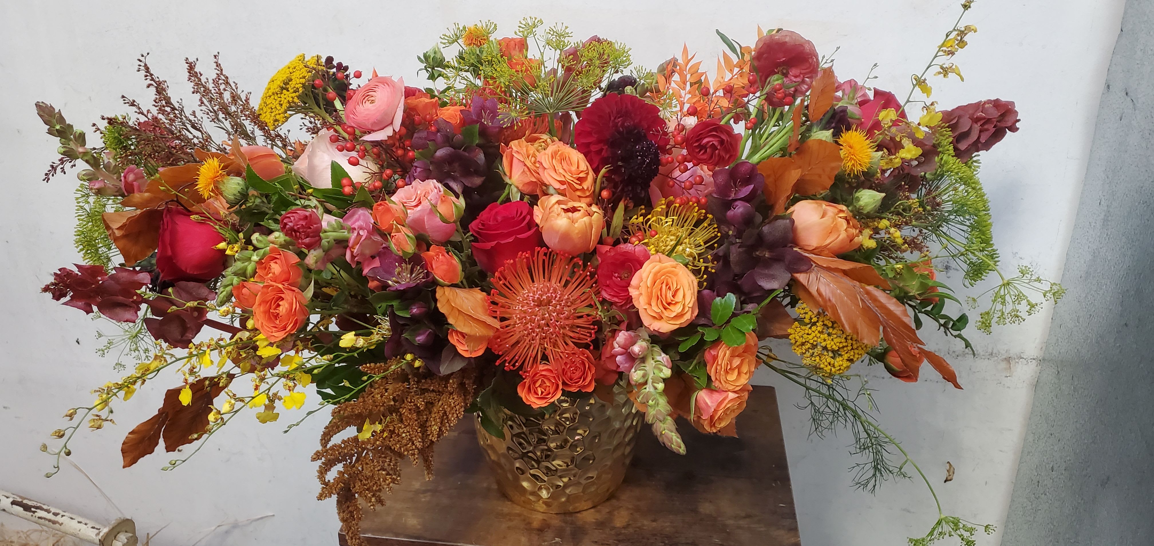 Large autumn bouquet with orange, red, and pink flowers in a gold vase