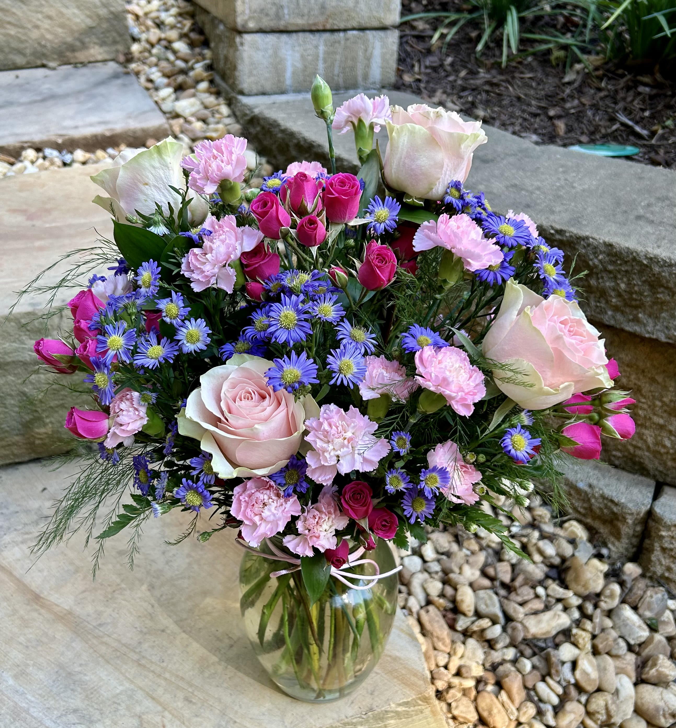 Bouquet of pink roses, carnations, and purple daisies in a glass vase