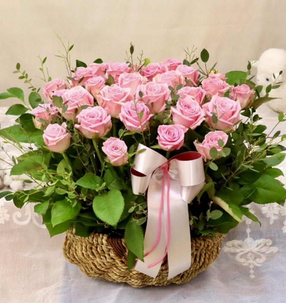 Pink roses arranged in a woven basket with a ribbon bow