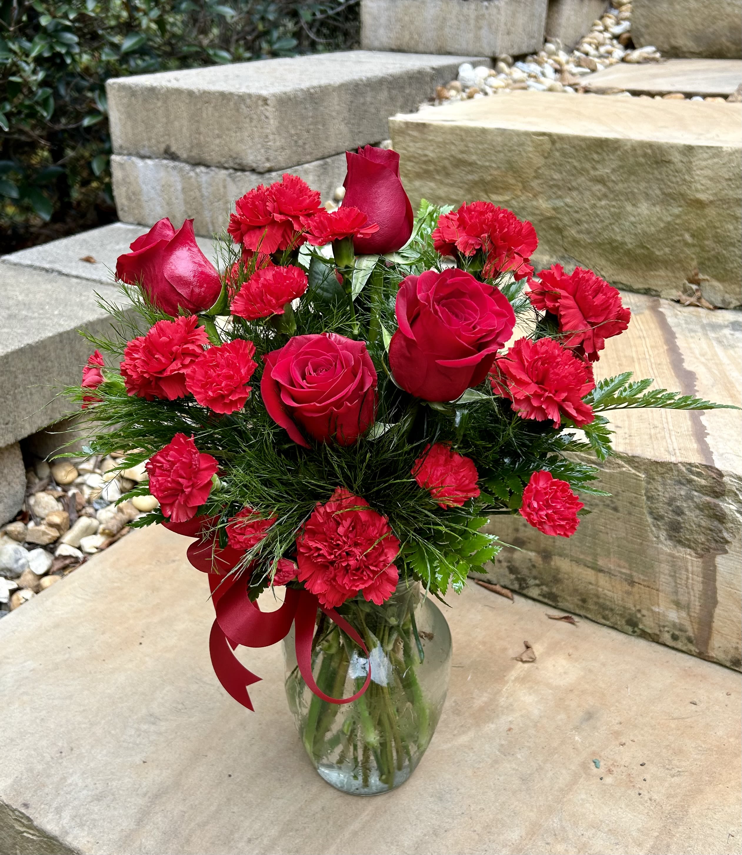 Red roses and carnations arranged in a clear glass vase with a red ribbon.