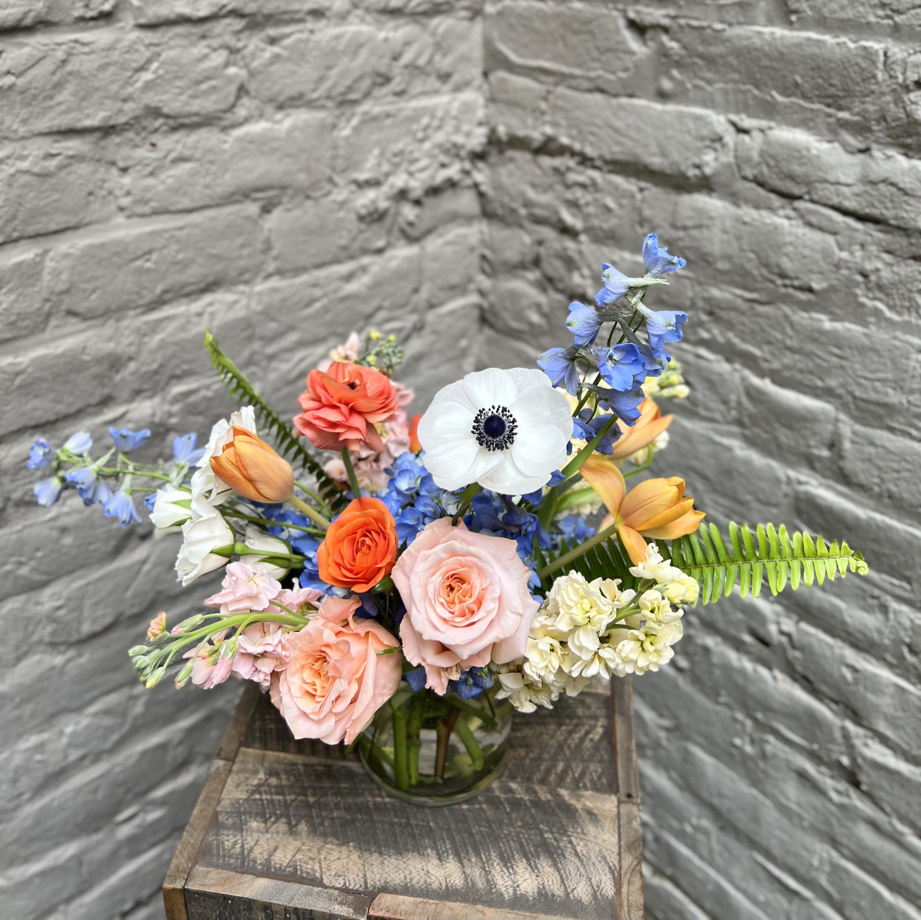 Mixed bouquet of roses, tulips, and blue flowers in a glass vase