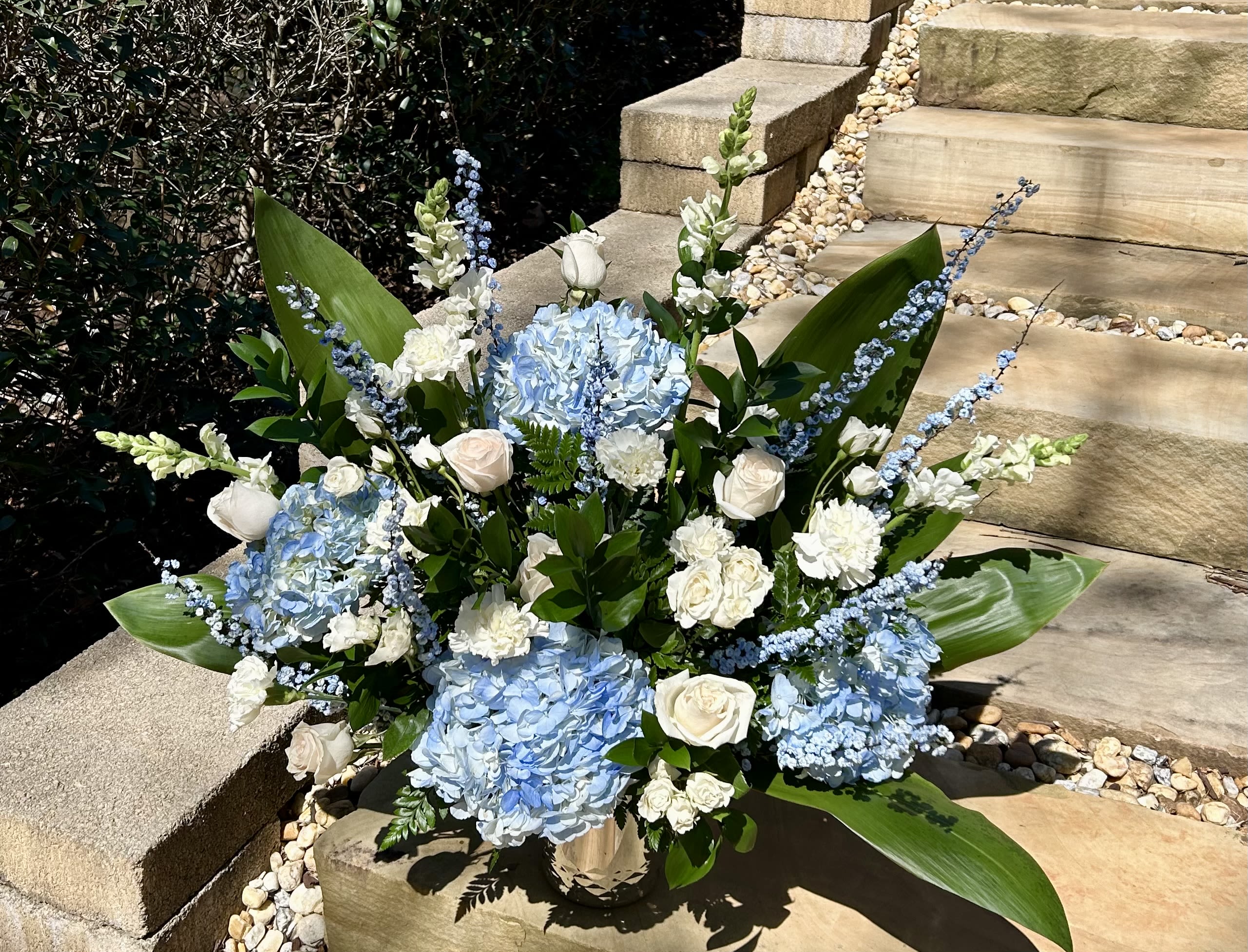 Blue hydrangeas and white roses arranged in a vase with tall blue accents