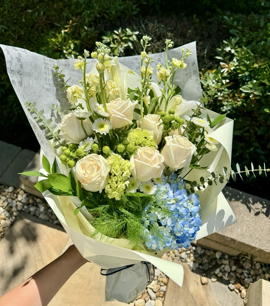 Bouquet of white roses, blue hydrangea, and green accents wrapped in paper