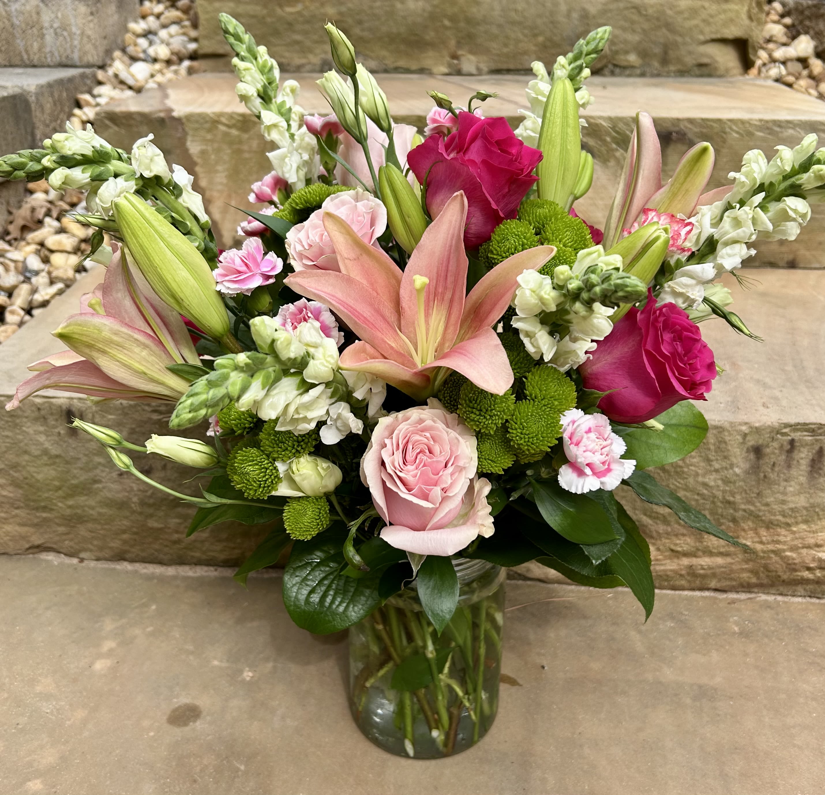 Bouquet of pink lilies, roses, and green button mums in a glass vase