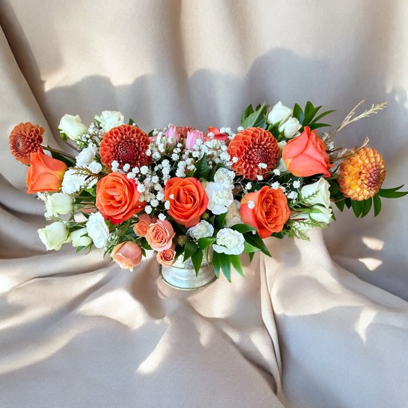 Sunset Serenity Bouquet #71 - The Sunset Serenity Bouquet is a stunning arrangement of vibrant orange roses and dahlias, complemented by delicate white mini carnations and gypsophila. Housed in a sleek metallic vase, this bouquet exudes elegance and warmth, making it a perfect choice for any occasion, from celebrations to expressions of appreciation. The blend of bright and soft hues creates a harmonious balance, evoking the tranquil beauty of a sunset.
